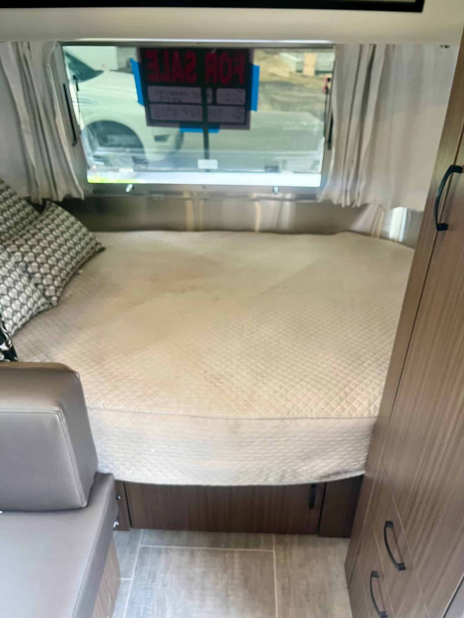 Spacious rv rental interior featuring a large, quilted bed, window with exterior view, and modern wood cabinetry.. Airstream Caraval 2021