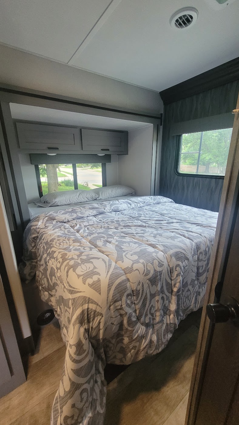 Cozy RV rental bedroom features a comfy bed with patterned bedding, overhead cabinets, and windows, offering a relaxing retreat.. Solera Solera Motorhome 2022