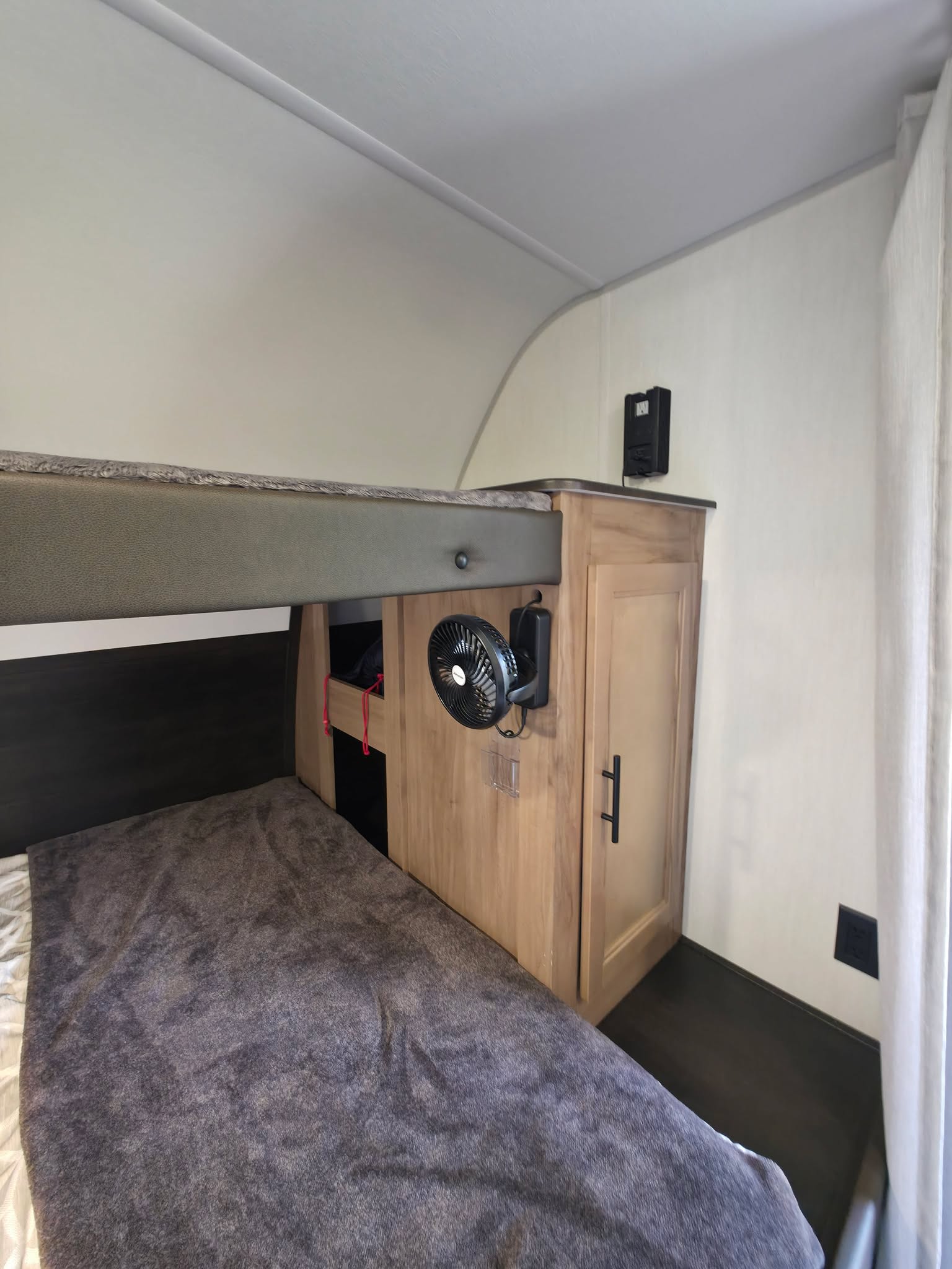 RV rental interior featuring a cozy lower bunk bed, a wooden cabinet, and a clip-on fan for comfort.. Forest River 19SM 2025