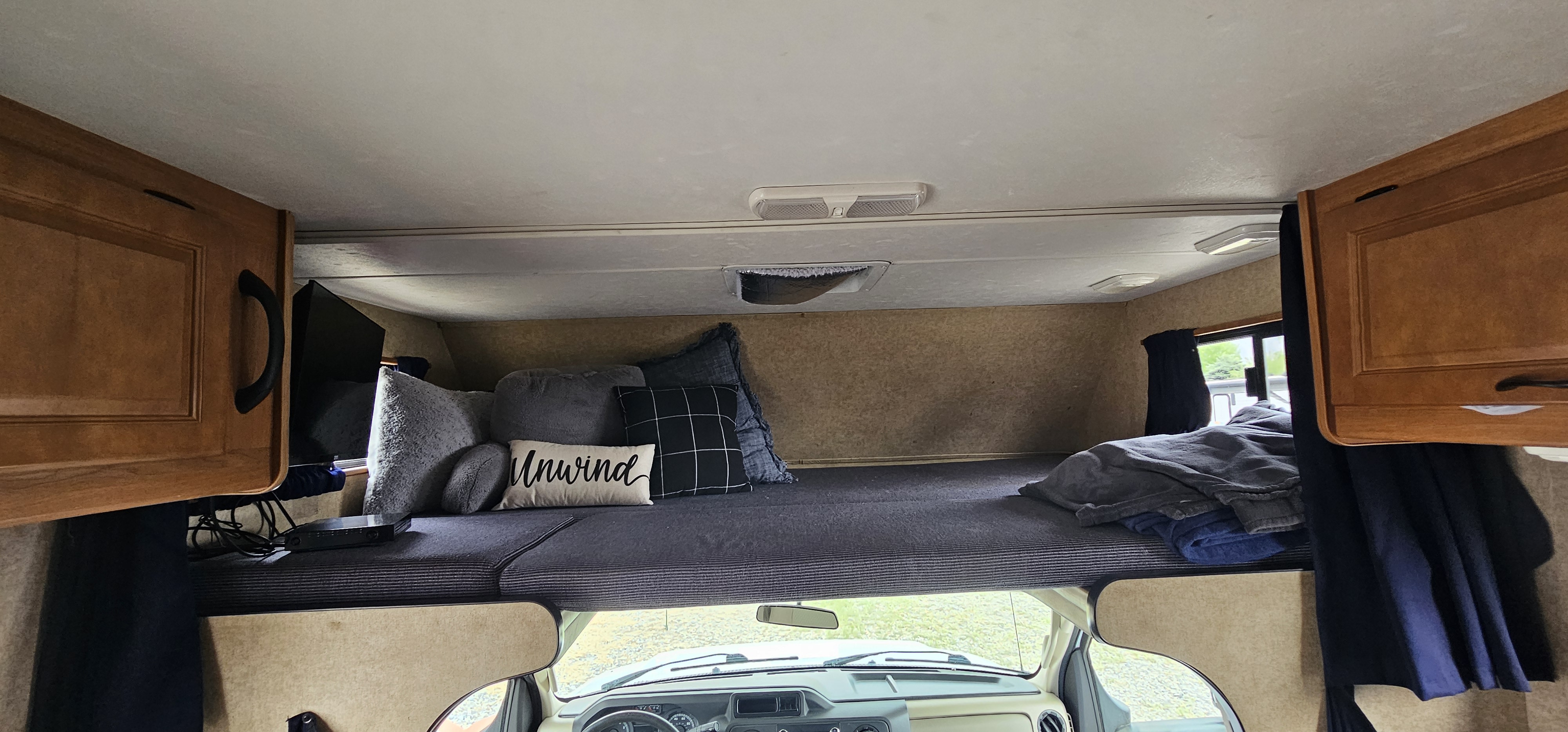 Cozy RV rental interior: cab-over bunk bed with pillows, blankets, storage cabinets, and a view of the road below.. Thor Majestic 2015