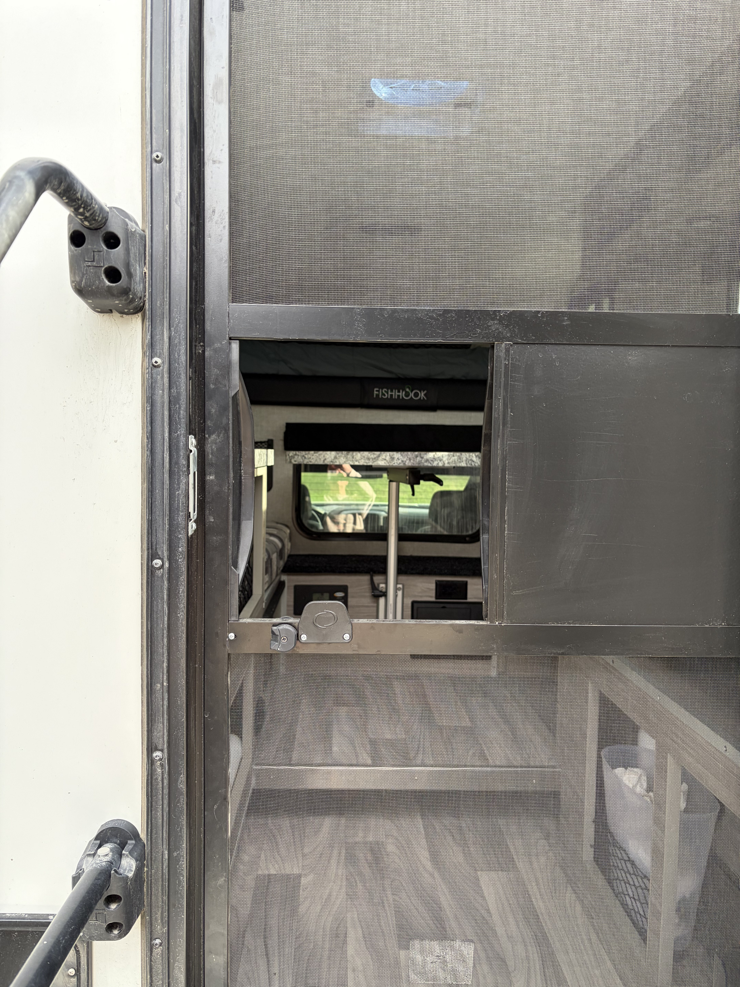 Inside an RV rental through a screen door: view of the interior with a "FISHHOOK" bunk, table, and flooring.. Custom Camper 2025