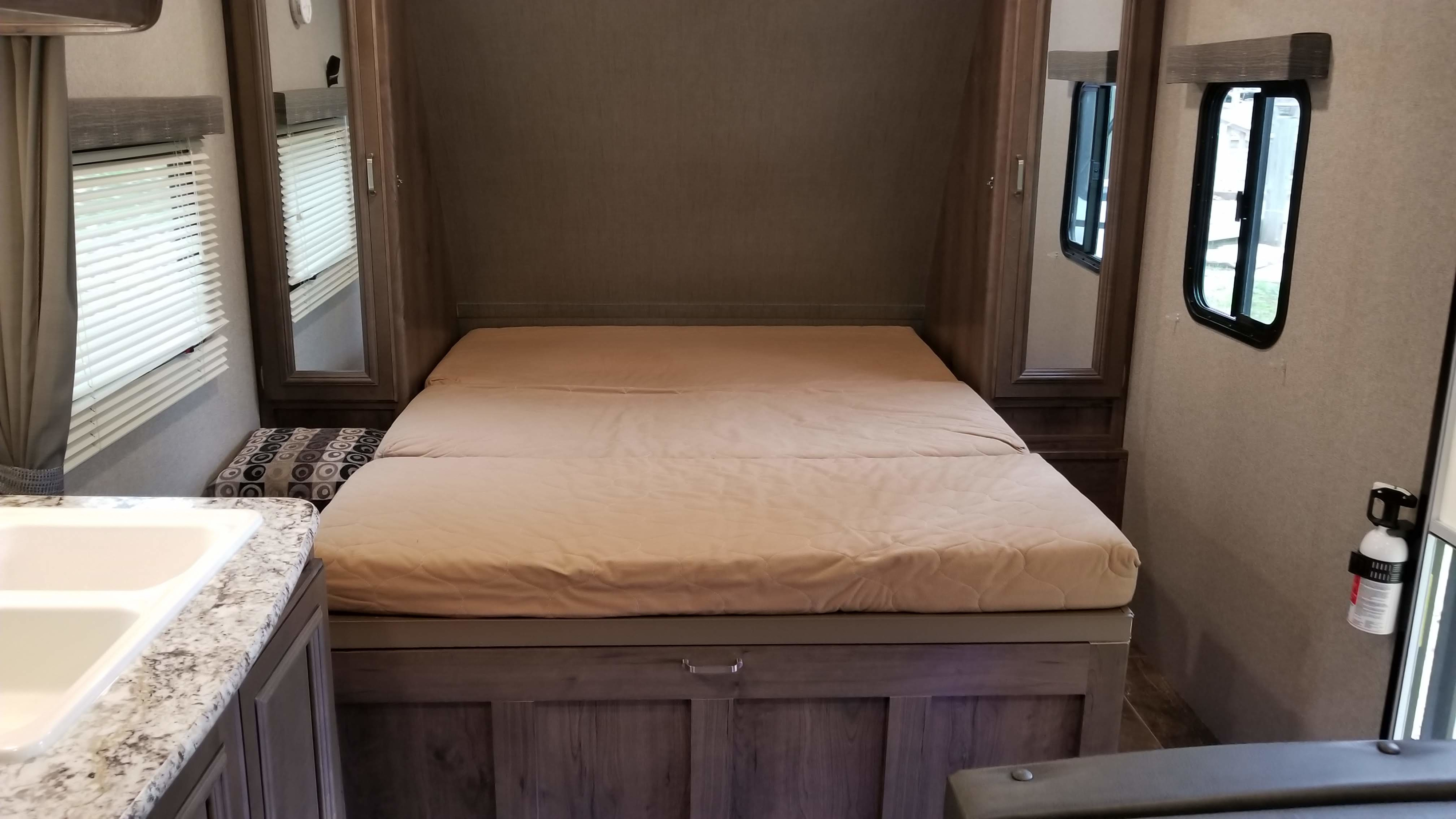 Discover this cozy rv rental bedroom, featuring a comfy bed, built-in storage, windows, and a sink area.. Keystone RV Passport Ultra Lite 2019
