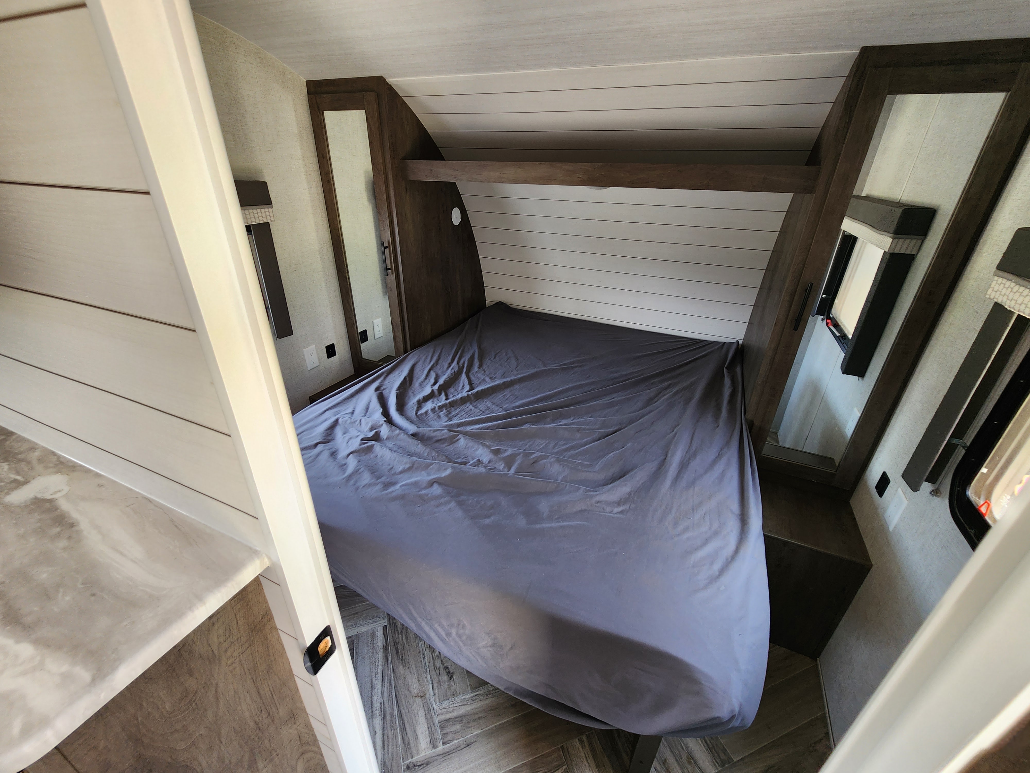 This RV rental bedroom offers a comfortable gray bed, modern wood cabinets, and a stylish white shiplap headboard.. Forest River Wildwood X-Lite 2021
