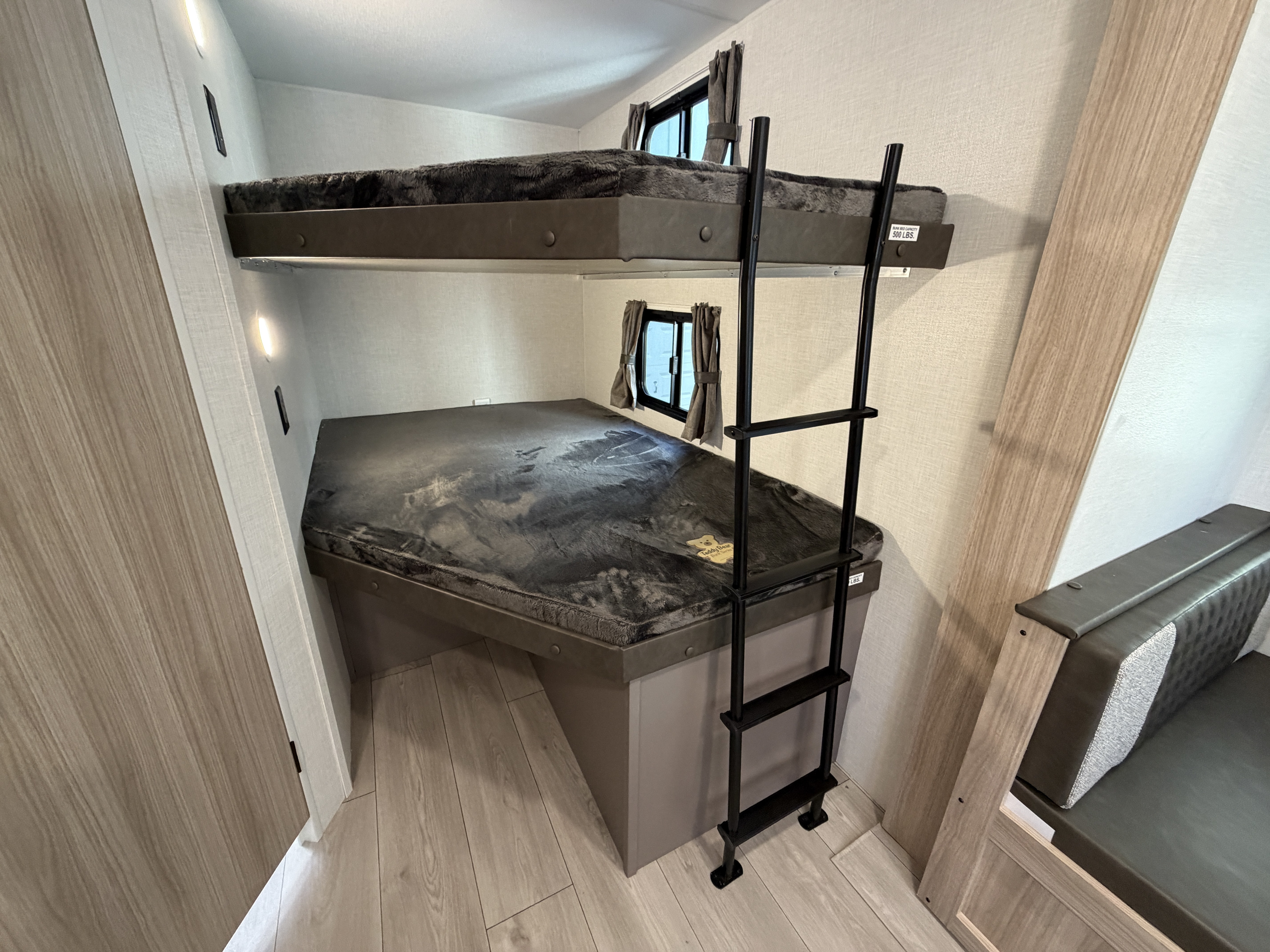 RV rental's interior: a double bunk bed setup with a ladder, plush gray mattresses, windows, and accent lights.. KZ Sportsmen SE 2026
