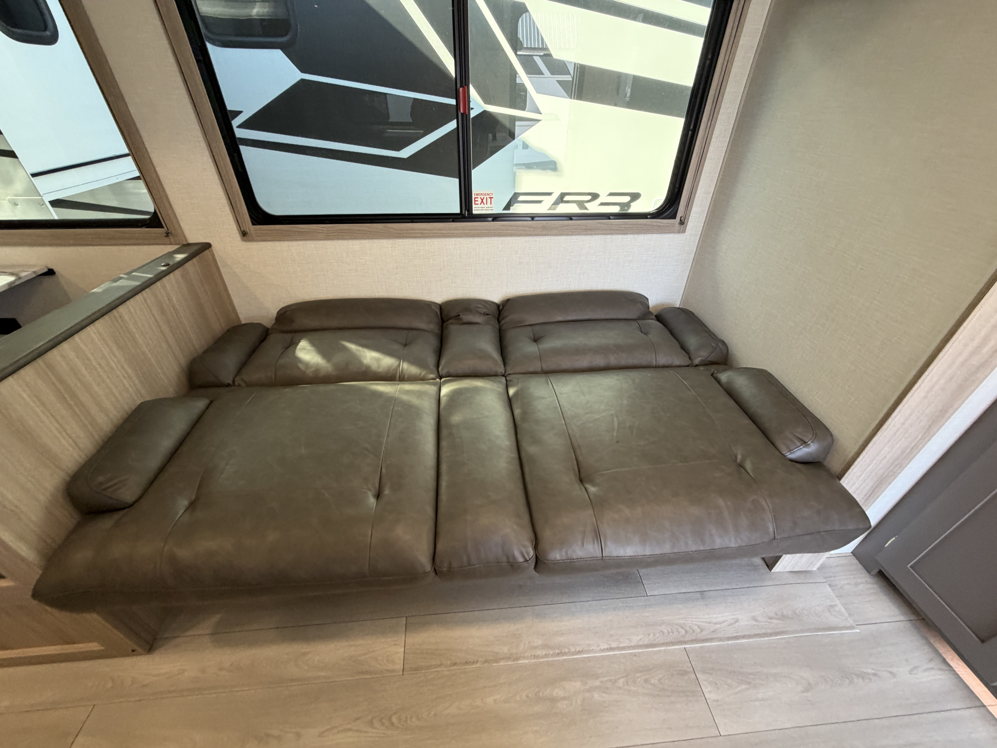 Inside an RV rental: a spacious brown upholstered sofa beneath a large window with an emergency exit visible. Ideal RV seating.. KZ Sportsmen SE 2026