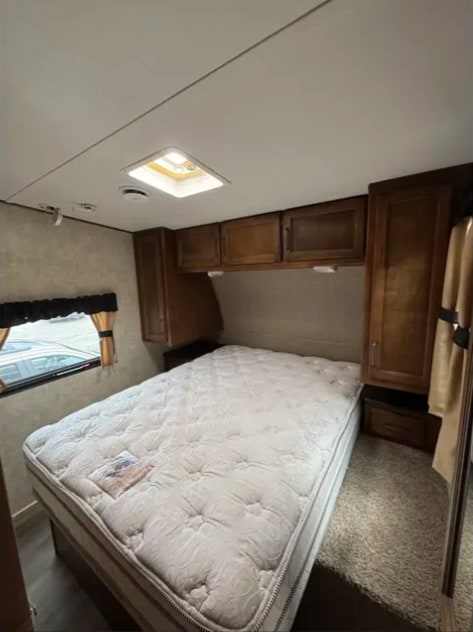 Cozy RV rental bedroom with a plush mattress, wooden cabinets, window, and ceiling skylight for natural light.. Keystone Carbon 2015