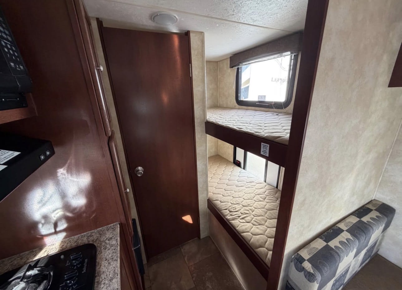 RV rental interior: bunk beds with quilted mattresses, a dark brown door, and a kitchen area with a stove and microwave visible.. Clipper Clipper Trailer 2014