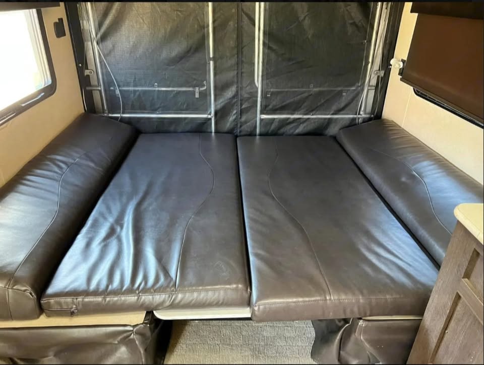 RV rental interior: A dark brown upholstered bed/seating area. Black fabric wall, window, and wood cabinetry.. Forest River Salem 2019