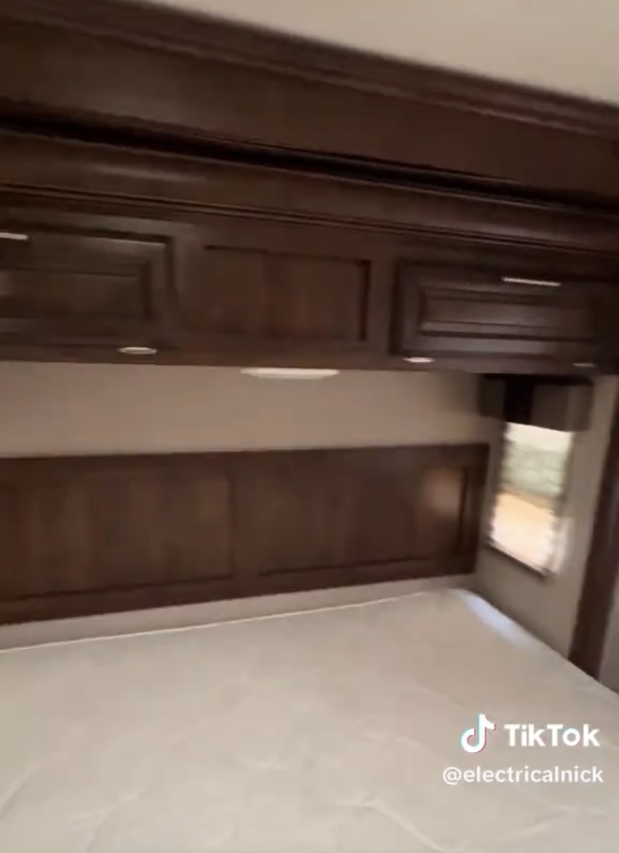 Inside an RV rental bedroom: dark wood overhead cabinets, headboard, and a clean white mattress, offering a compact, cozy interior.. Forest River FR3 2015