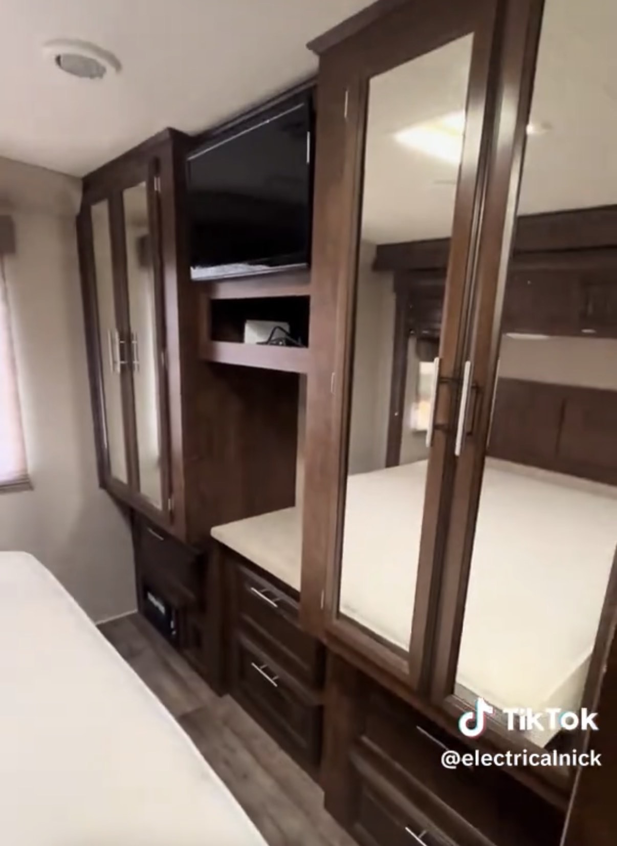 Compact RV rental bedroom with dark wood cabinetry, integrated TV, mirrored closets & drawer storage for efficient travel.. Forest River FR3 2015