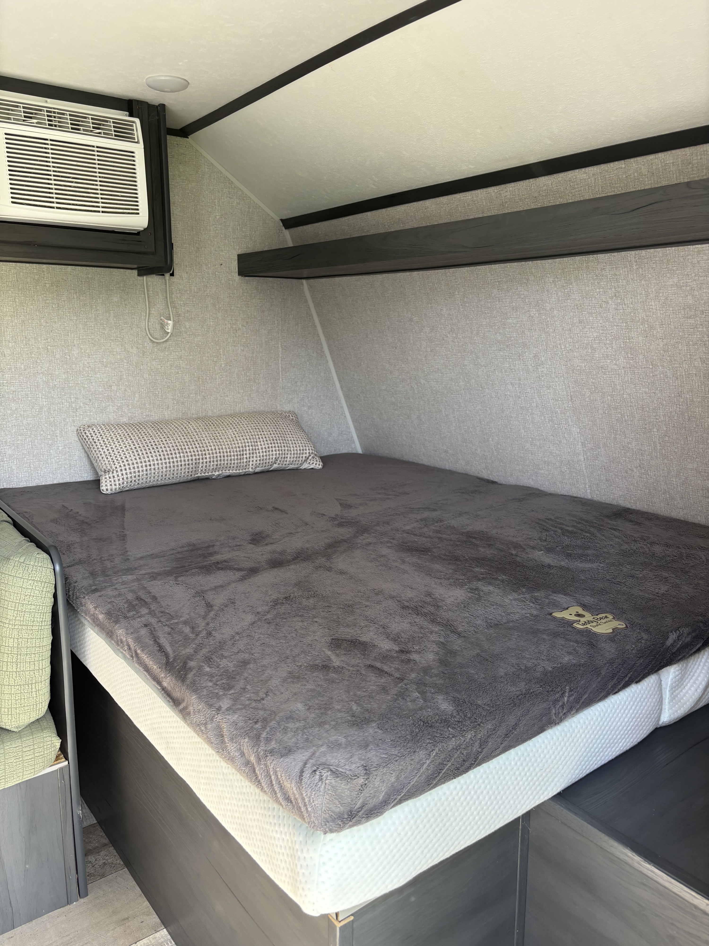RV rental bedroom featuring a bed, pillow, wall-mounted AC unit, and overhead shelf. Cozy space for travel.. Dutchmen Aspen Trail 17BH 2022
