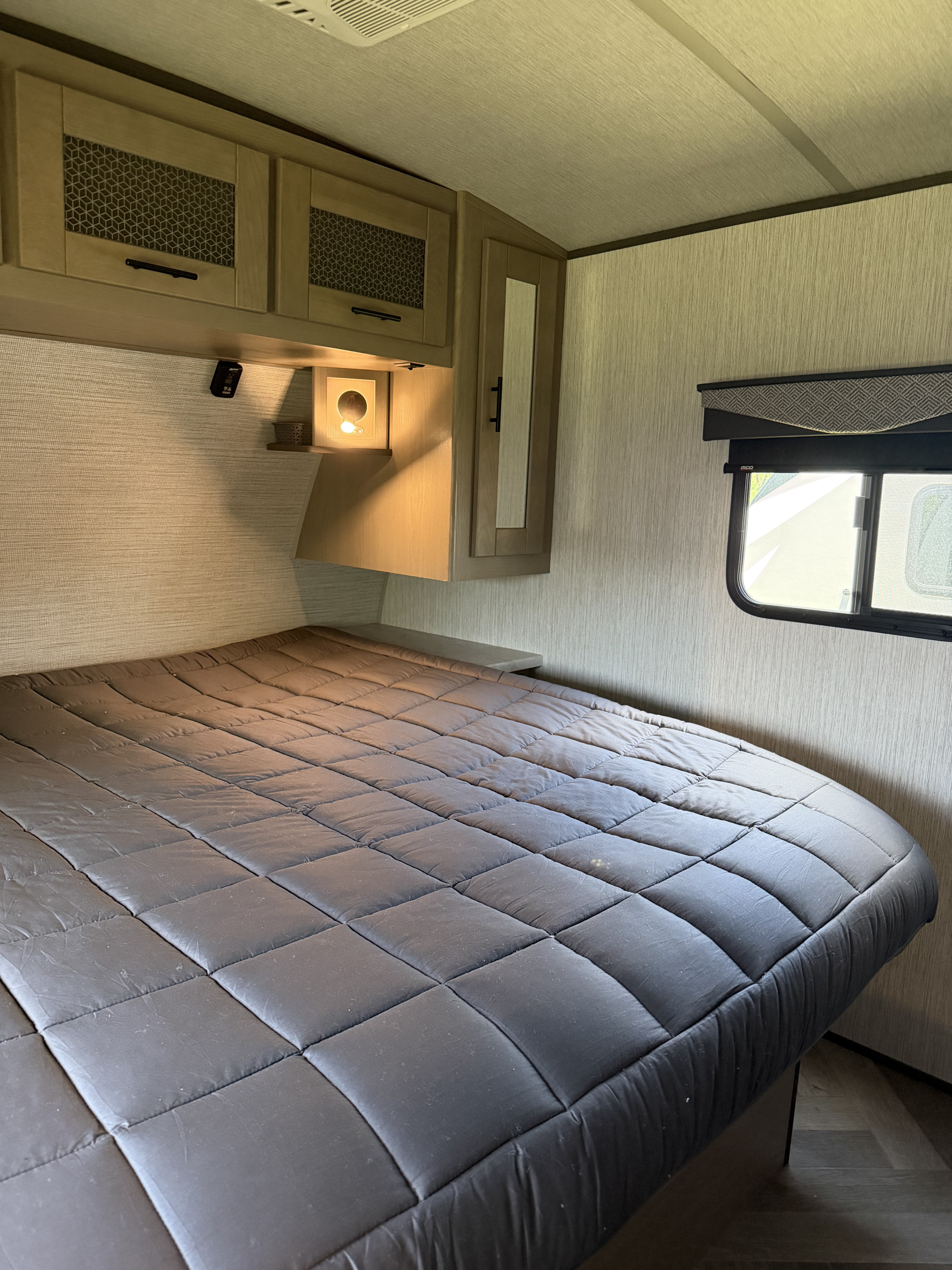 Cozy RV rental bedroom with a quilted bed, overhead cabinets, and a window, designed for comfort.. Cruiser RV Twilight Signature 2021