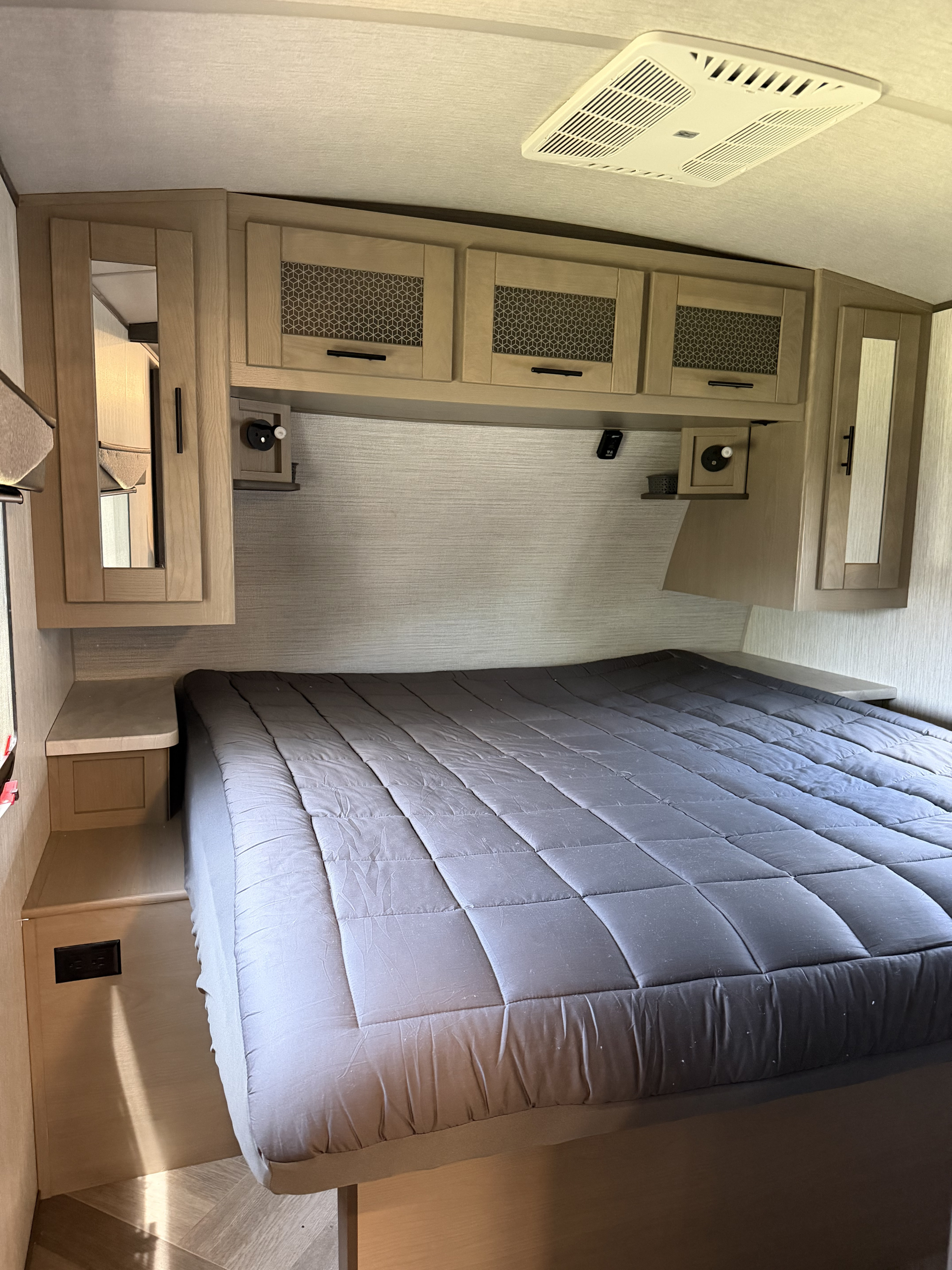 RV rental bedroom with a cozy bed, light wood overhead cabinets, side mirrors, and a ceiling-mounted AC unit.. Cruiser RV Twilight Signature 2021