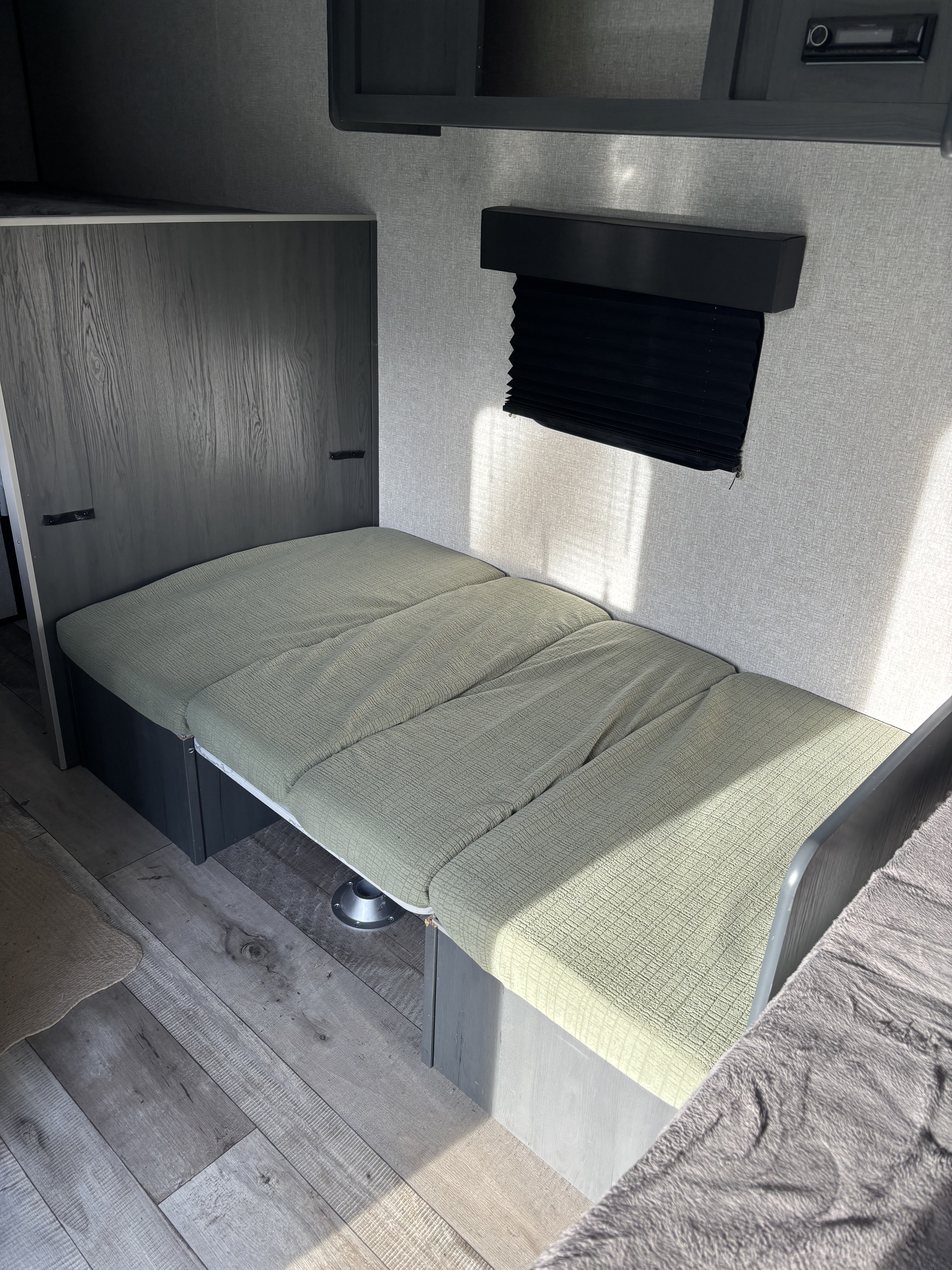 RV rental interior: Convertible dinette bench with light green cushions, folded into a bed configuration.. Dutchmen Aspen Trail 17BH 2022