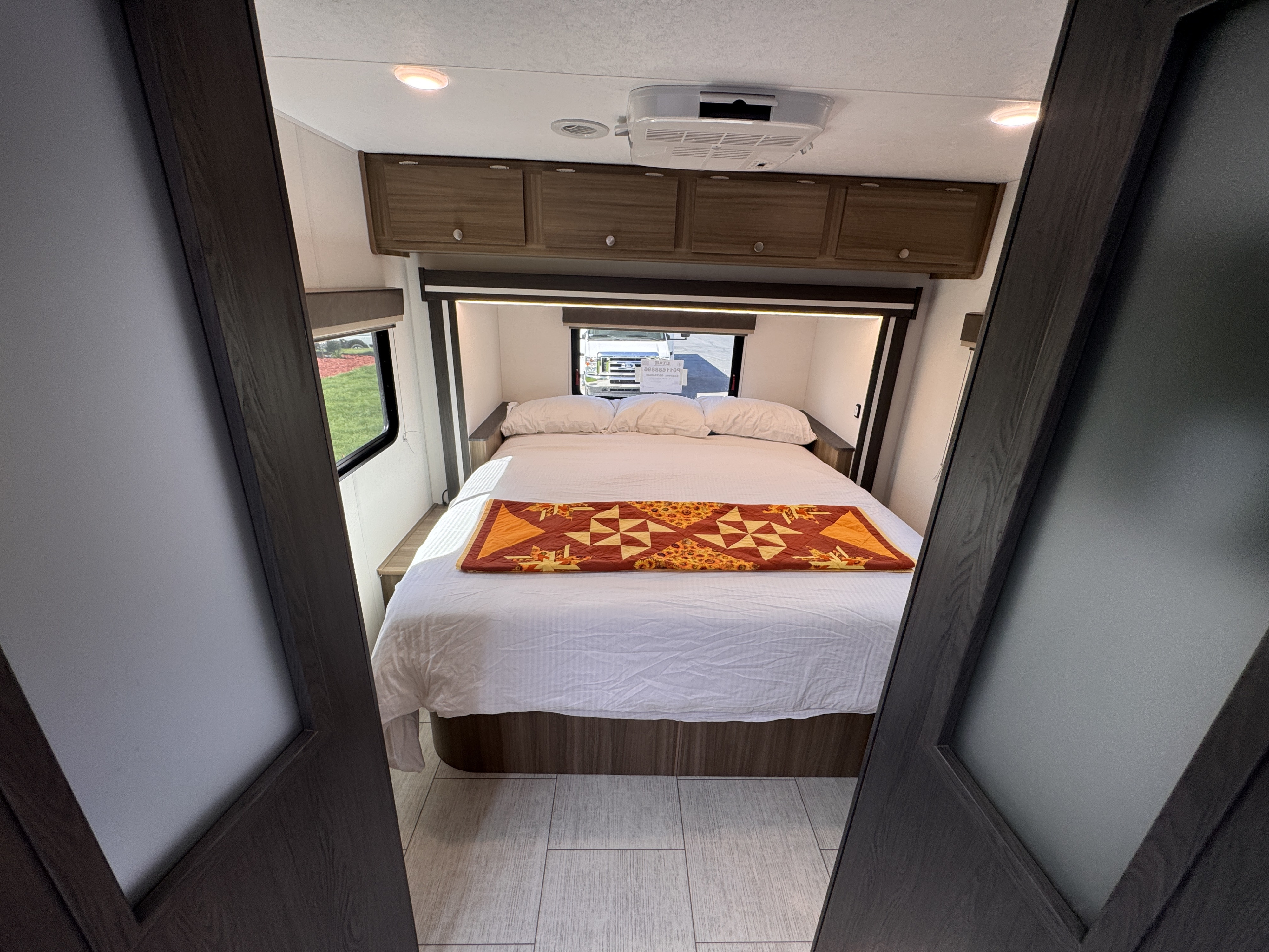 RV rental: inviting bedroom with a comfy bed, colorful quilt, overhead storage, AC, and bright windows for a relaxing trip.. Forest River Coachmen Freelander 2026