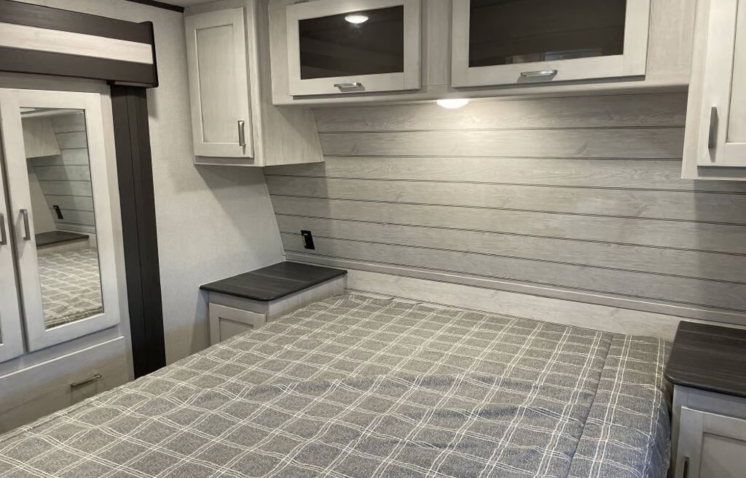 Comfortable RV rental bedroom featuring a plaid bed, wood-paneled headboard, and overhead storage with a mirrored closet.. Keystone RV Sprinter 2022