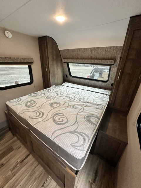 RV rental bedroom with a large bed, patterned mattress, side windows, and built-in storage cabinets.. KZ Escape 2019