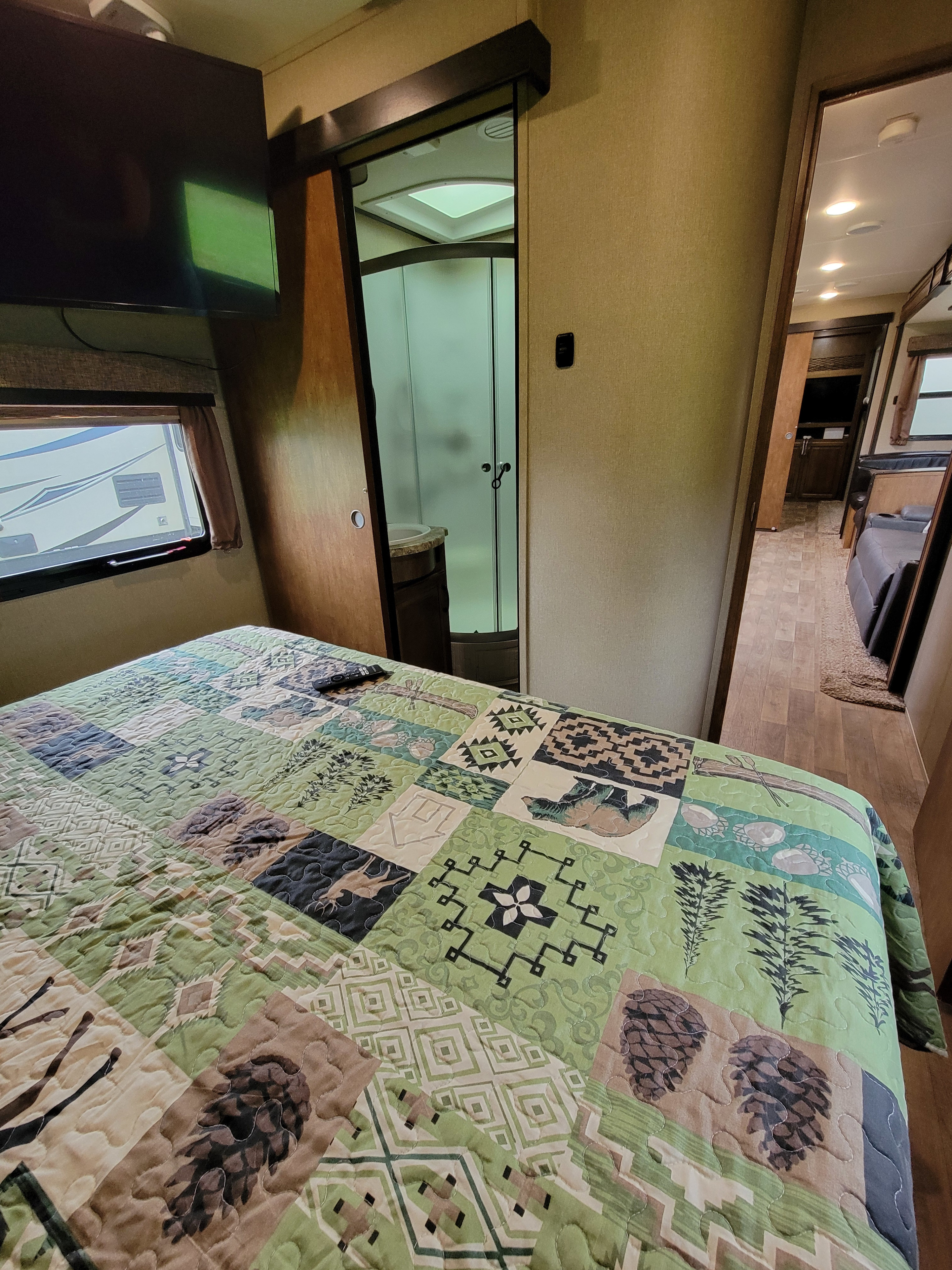 RV rental bedroom: cozy space with green quilt, TV, and en-suite shower. Hallway leads to main living area.. Grand Design Reflection 2017