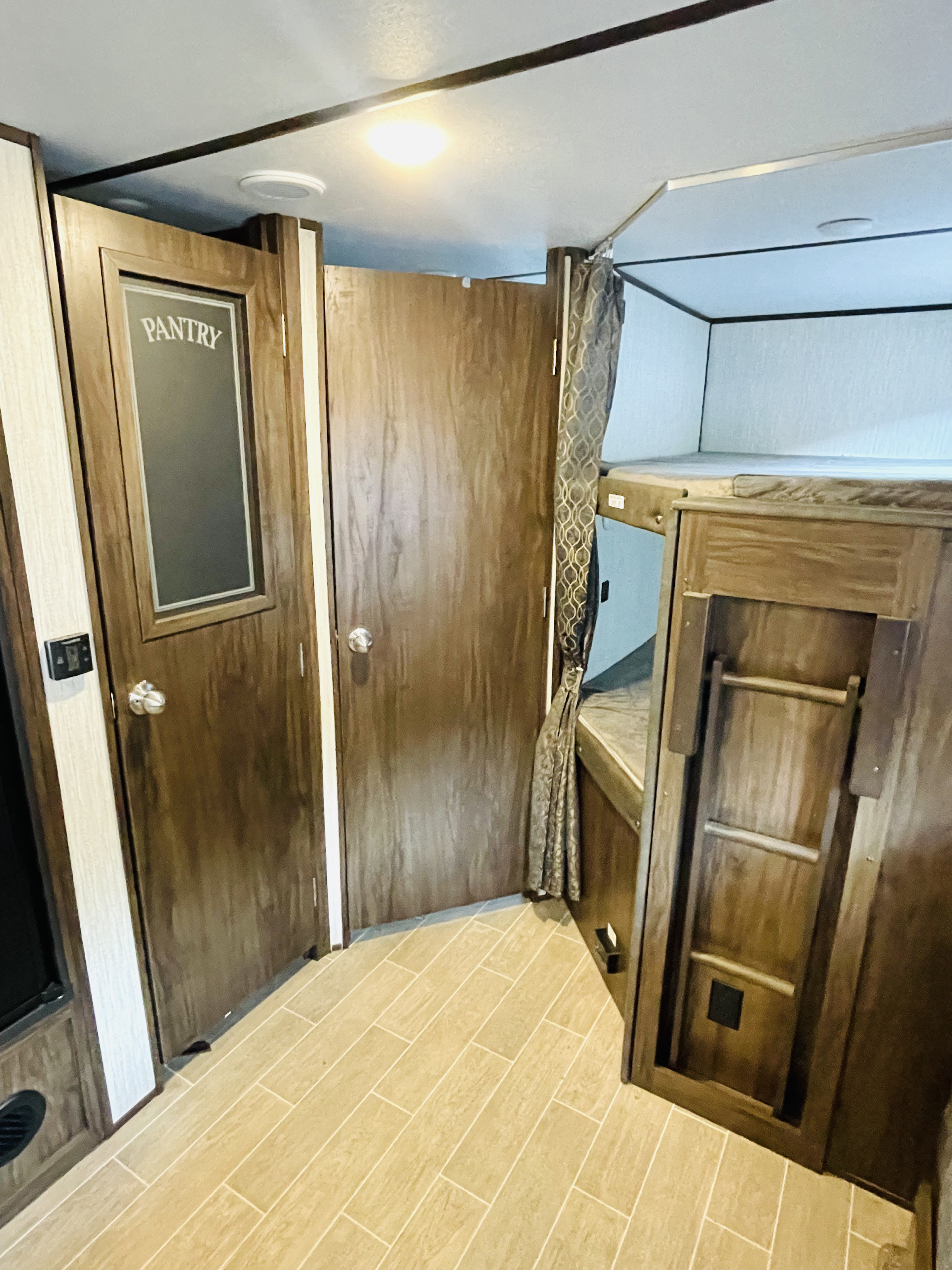 Inside an RV rental: view of a pantry door, another door, and bunk beds with a ladder in a compact space.. Forest River Cherokee Alpha Wolf 2019