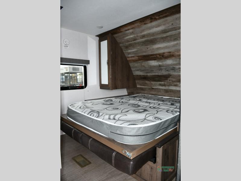 RV rental bedroom with a bed, rustic wooden headboard, window, and mirrored cabinet.. Keystone RV Passport SL 2020