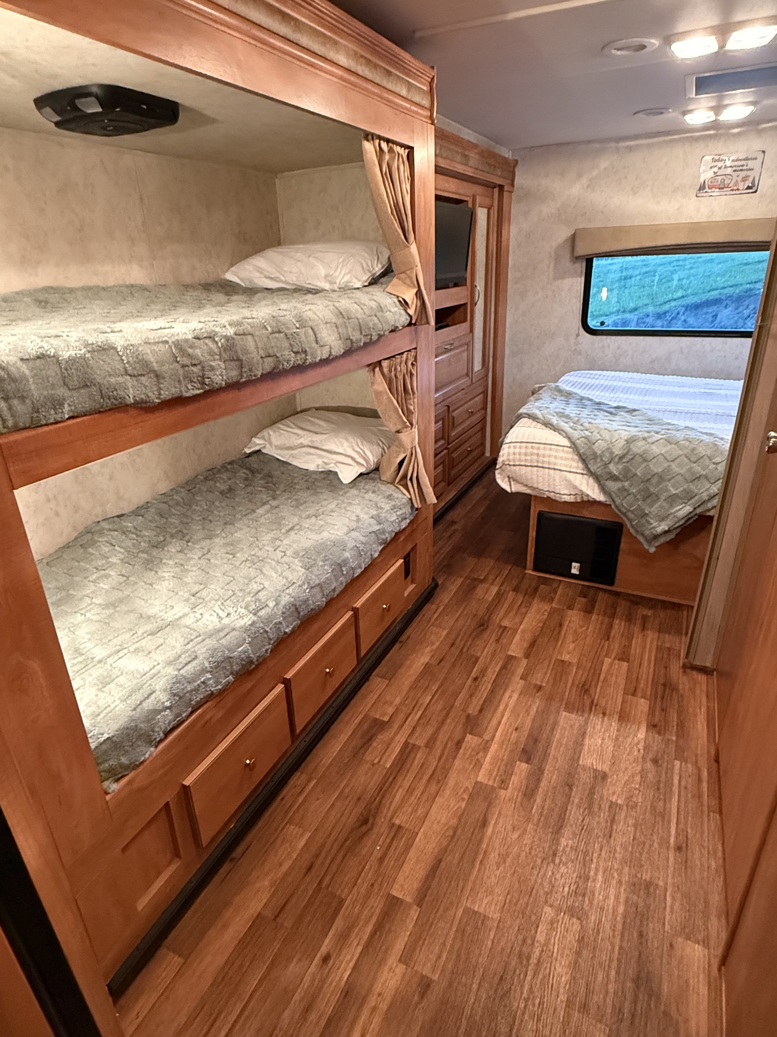 Cozy RV rental bedroom featuring bunk beds with storage drawers and a comfortable main bed by a window.. Nexus RV Phantom 2014