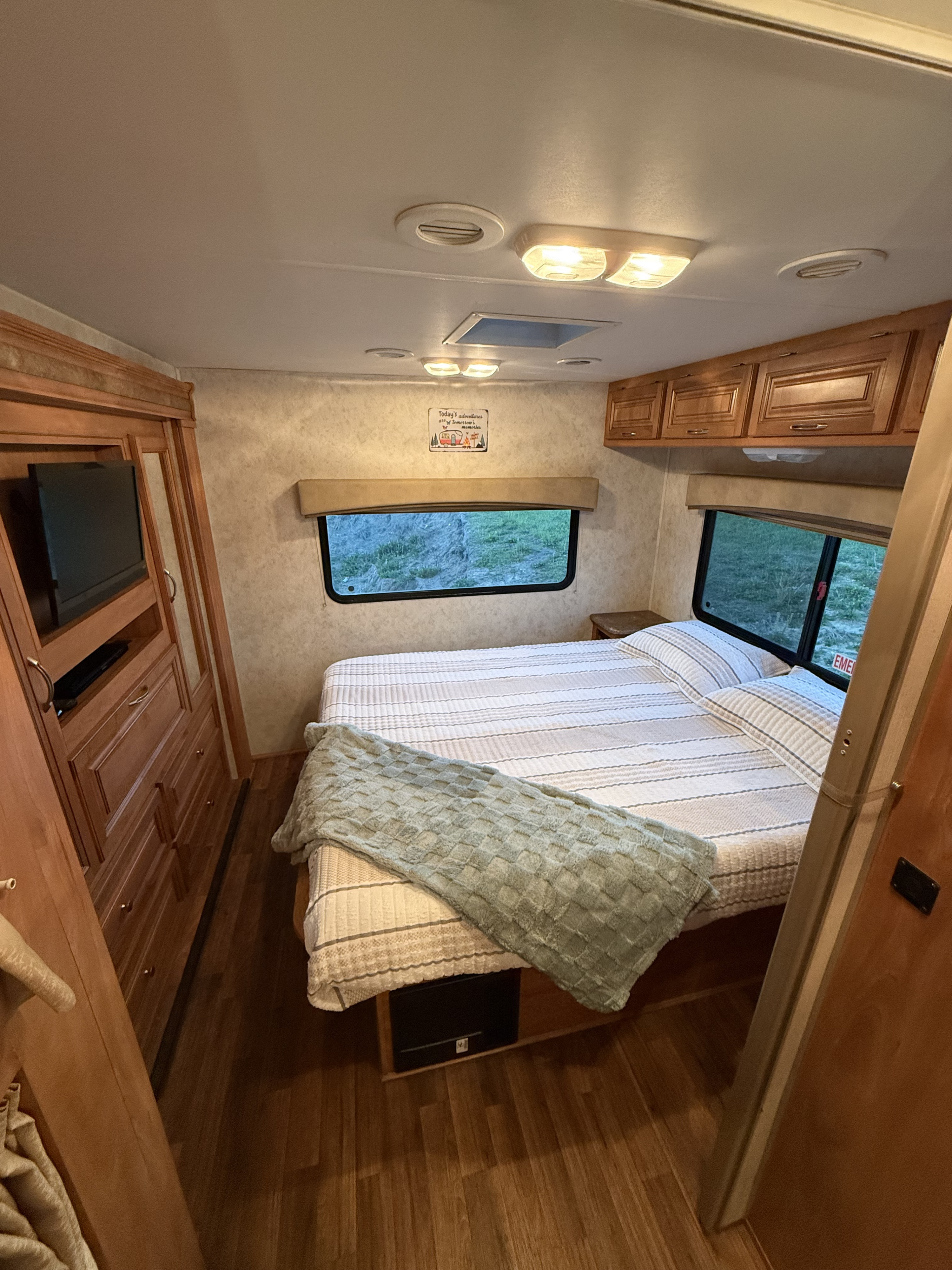 Cozy RV rental bedroom with striped bedding, a window view, wood cabinets, and built-in TV for comfortable travel.. Nexus RV Phantom 2014
