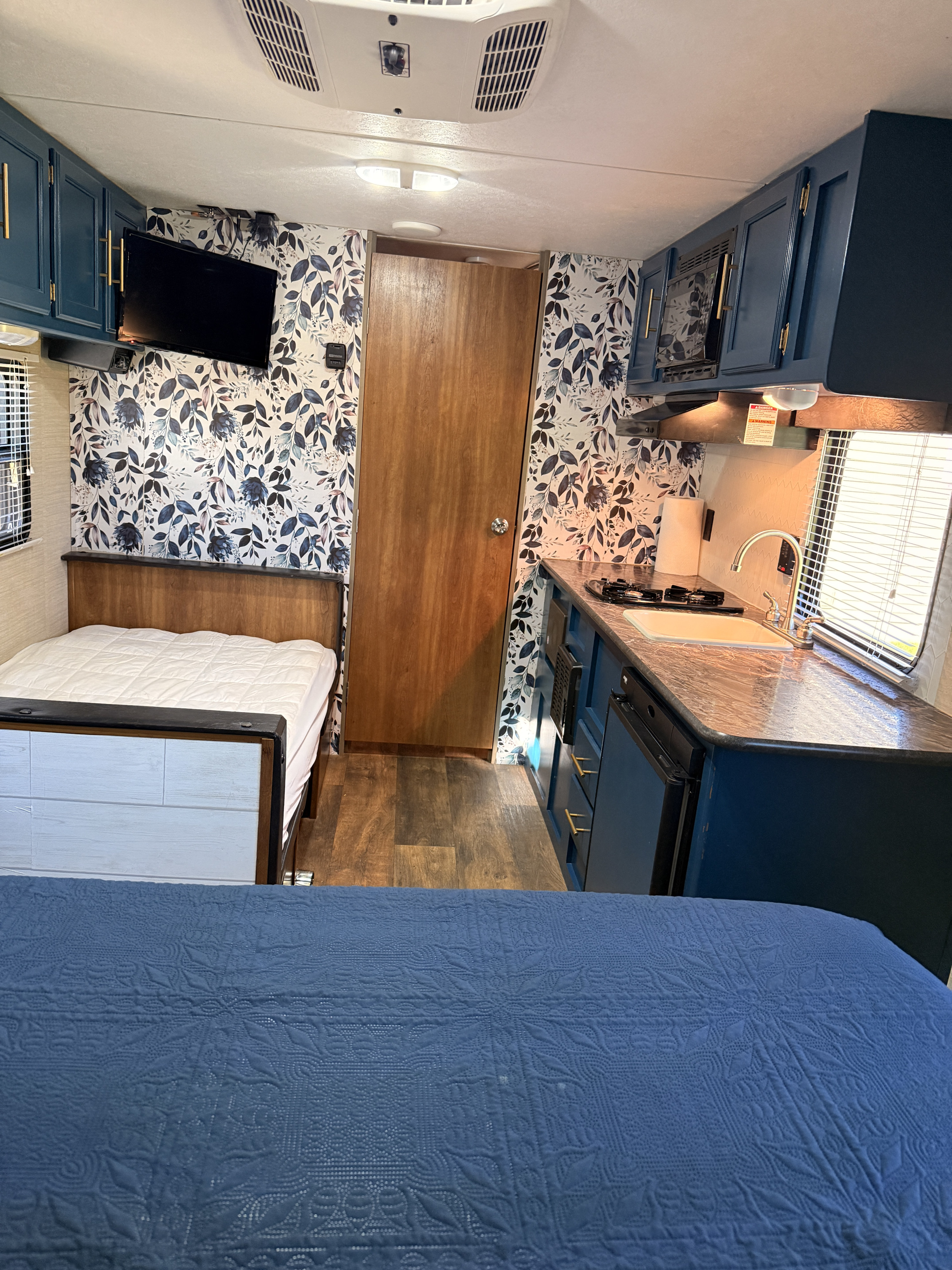 Cozy rv rental interior with renovated blue cabinets, floral wallpaper, a kitchenette, and sleeping area.. Keystone RV Summerland Mini 2016