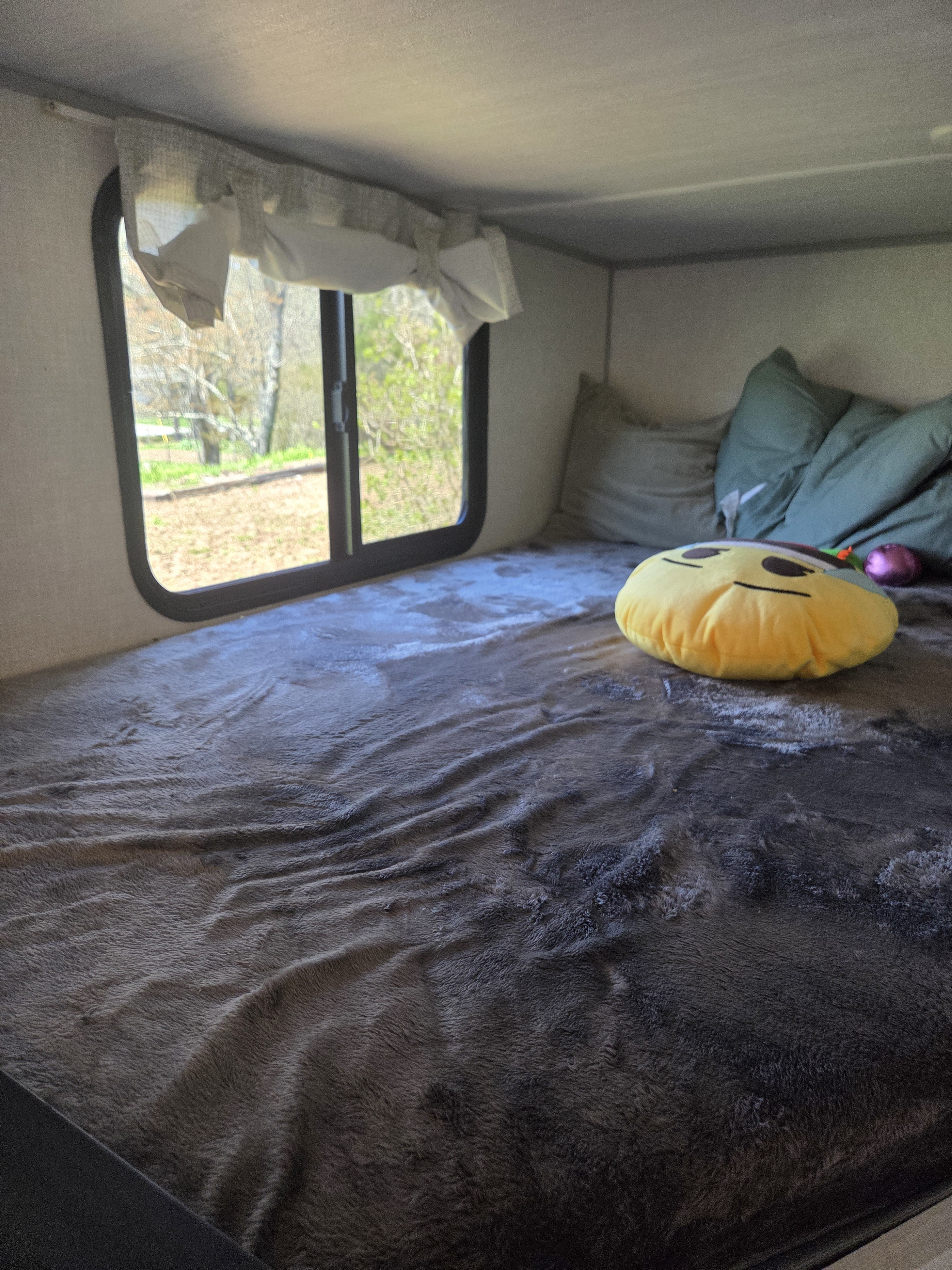 Comfy RV rental sleeping area featuring a plush blanket, yellow pillow, and a window framing a view of nature.. No Boundaries 19 Essentials Only 2024