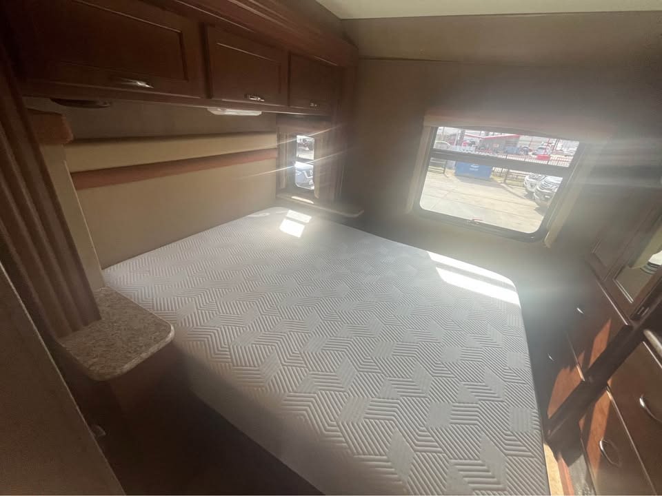 Your cozy RV rental bedroom features a comfortable bed, dark wood cabinets, and a bright window view.. Thor Motor Coach A.C.E 2015