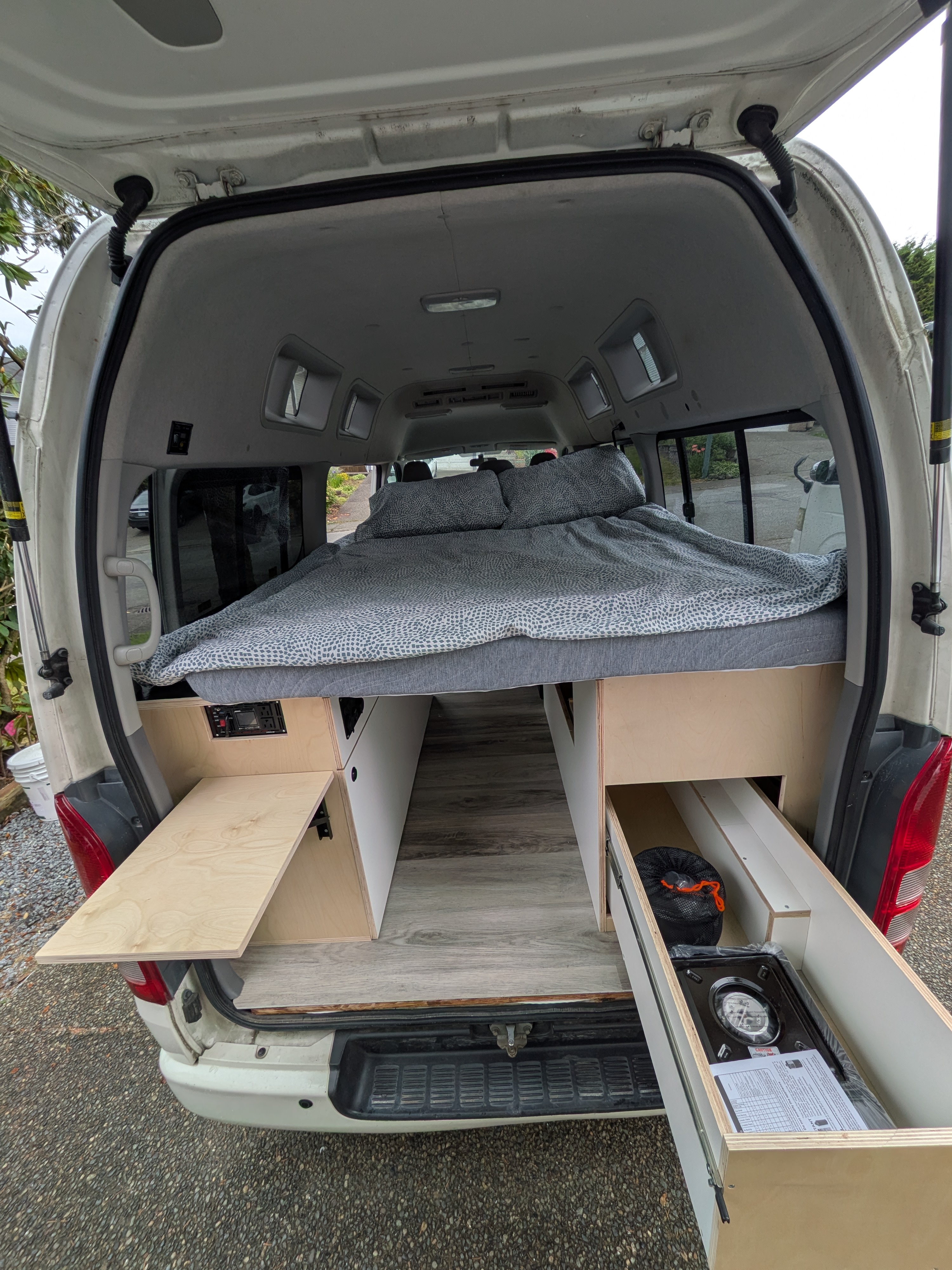 Inside an RV rental camper van: a cozy bed, pull-out counter, and rear kitchen drawer with stove. Functional van conversion.. Toyota Hiace 4WD 2009