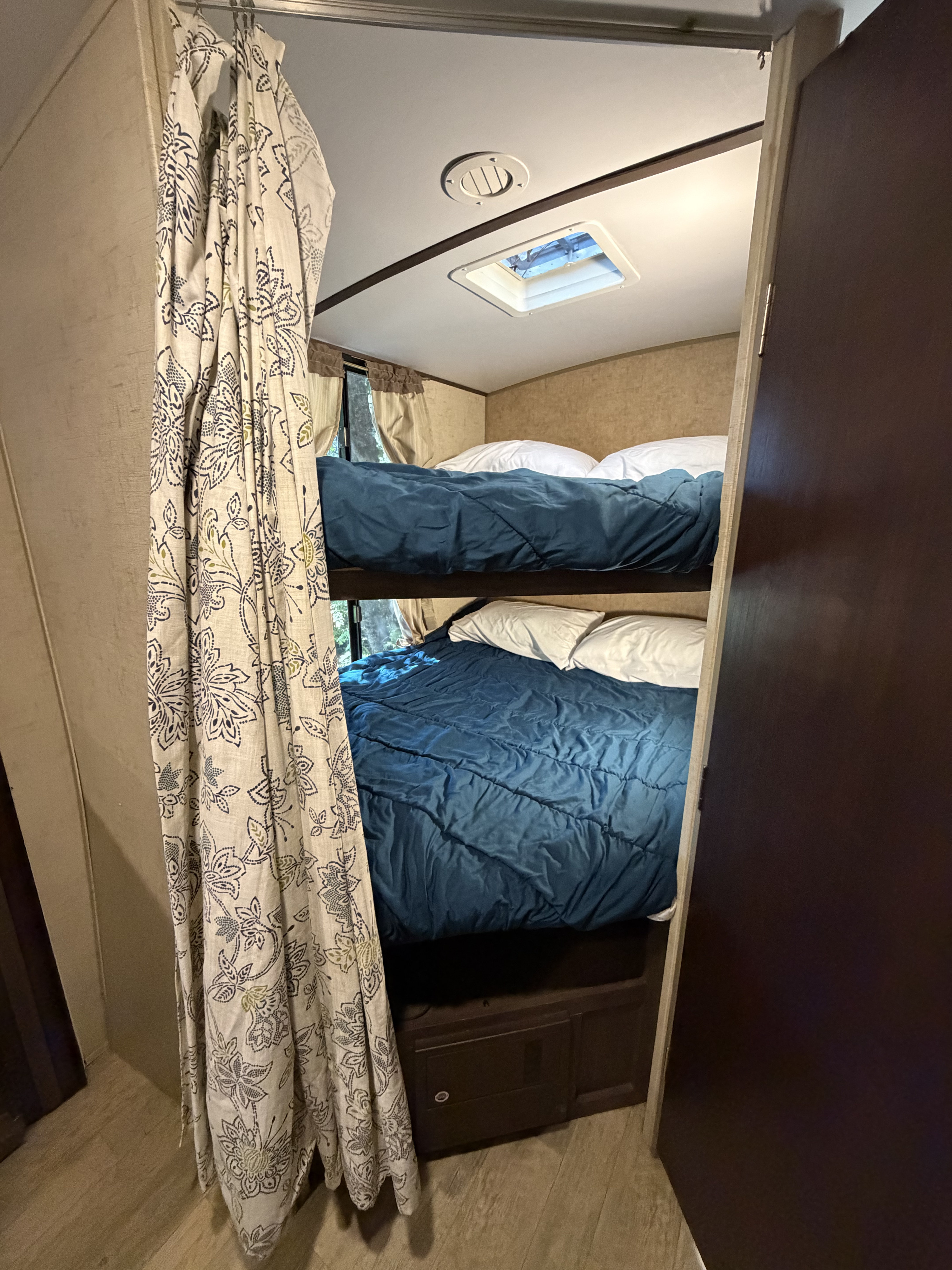 Cozy RV rental bunk beds, each with blue bedding. A patterned curtain offers privacy in this compact camper sleeping area.. Forest River Surveyor 2017