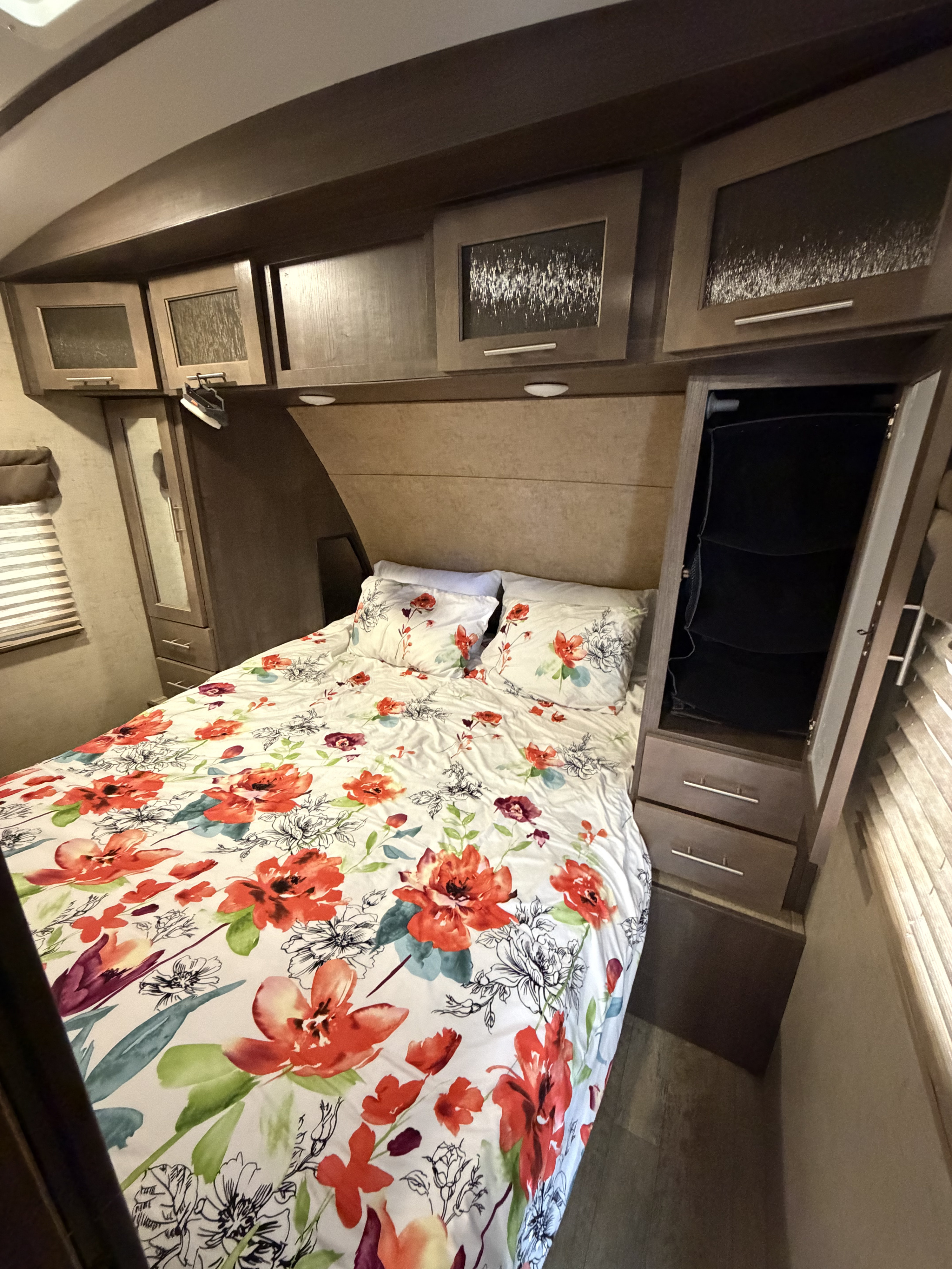 Bright RV rental bedroom with vibrant floral bedding, wood cabinets, and built-in storage for a relaxing journey.. Forest River Surveyor 2017