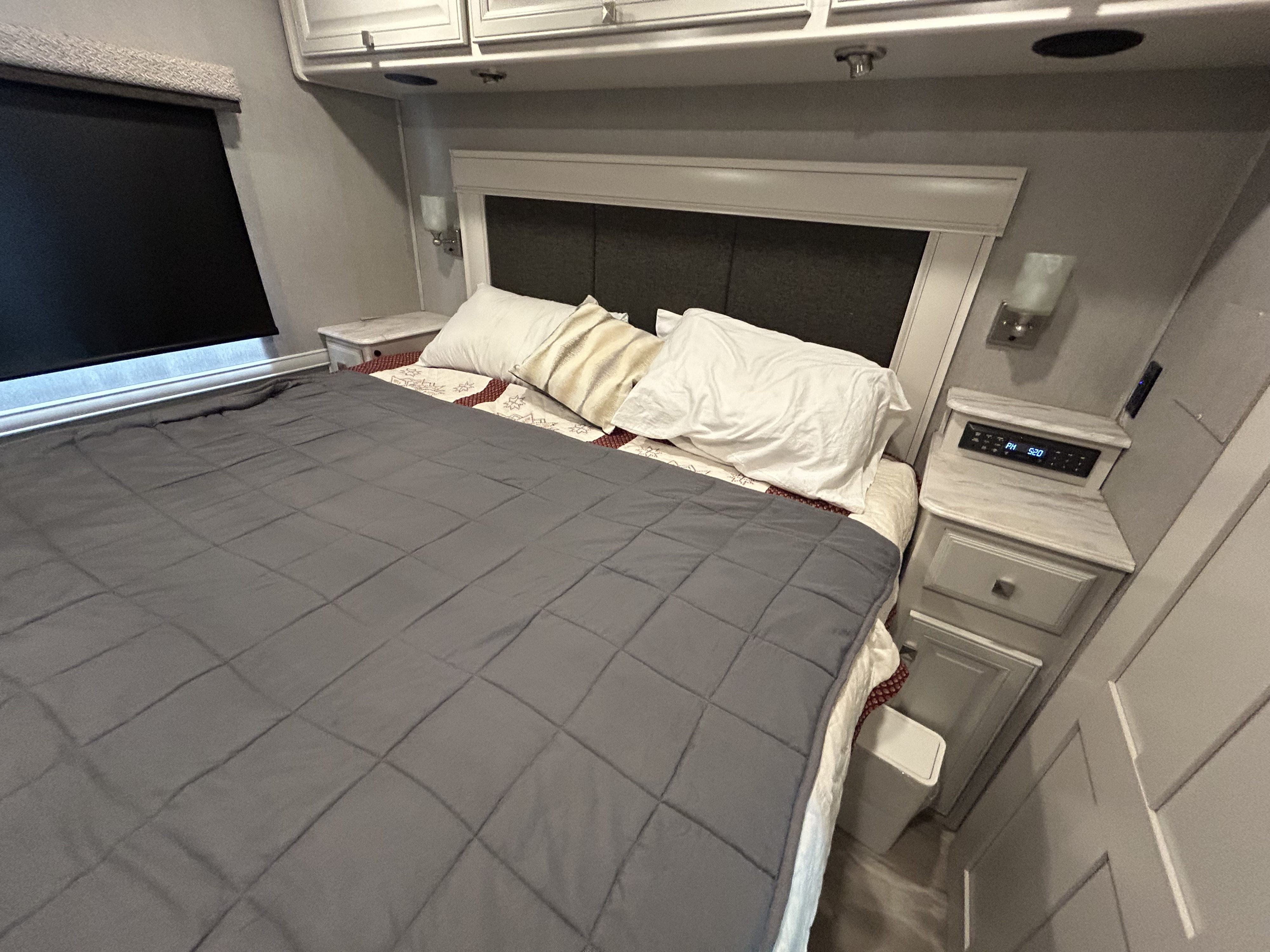 Experience comfort in this RV rental bedroom: a cozy bed with a grey comforter, pillows, and nightstands.. Holiday Rambler Admiral 2021