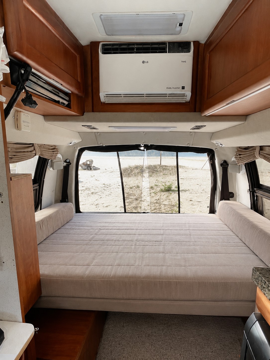 RV rental interior featuring a comfy bed, LG AC unit, and a scenic beach view from the rear of the camper van.. Roadtrek Roadtrek Class B 2008