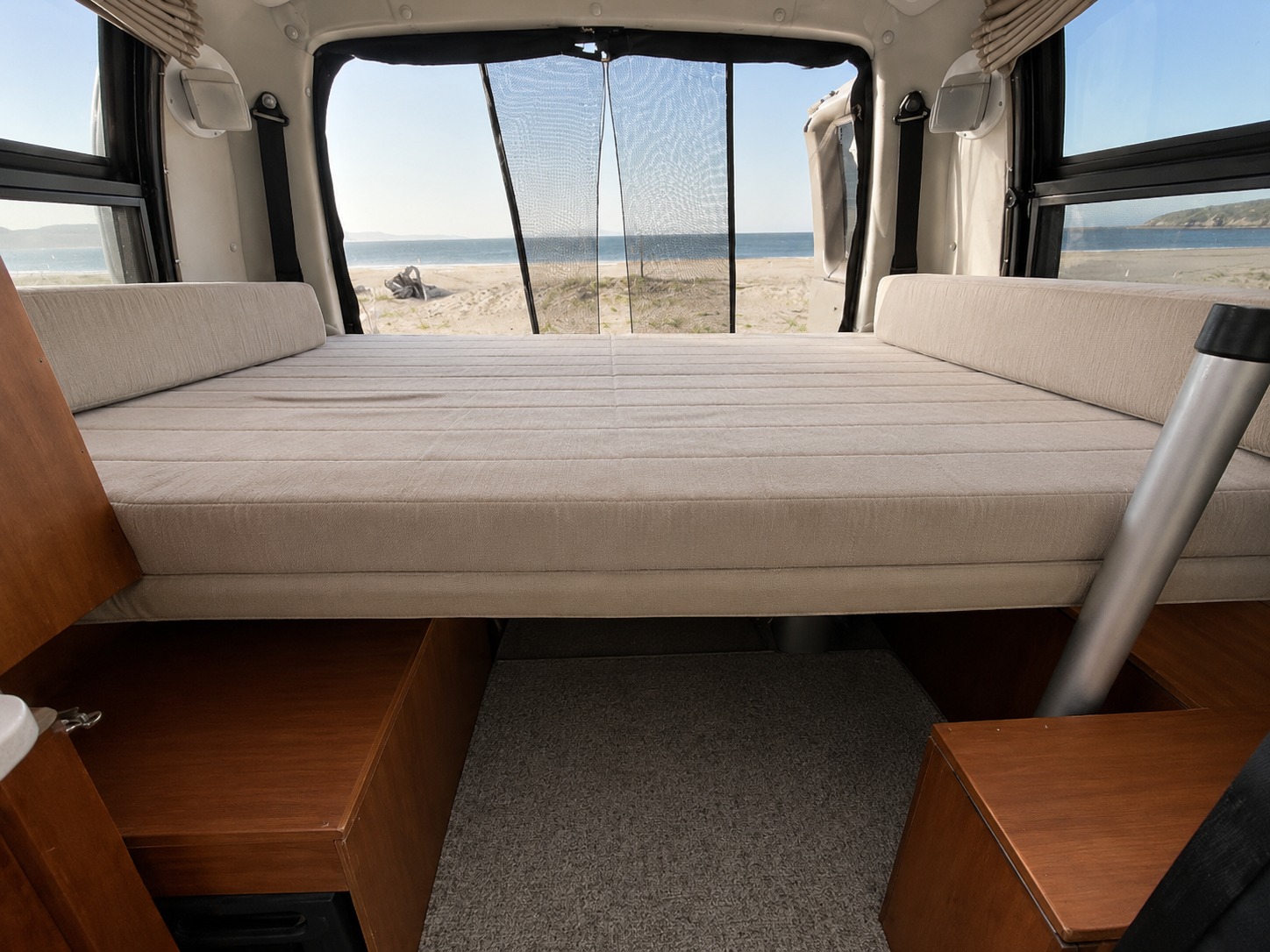 Inside an rv rental: A comfy bed provides a clear view of a sandy beach and ocean through the rear doors with mesh.. Roadtrek Roadtrek Class B 2008