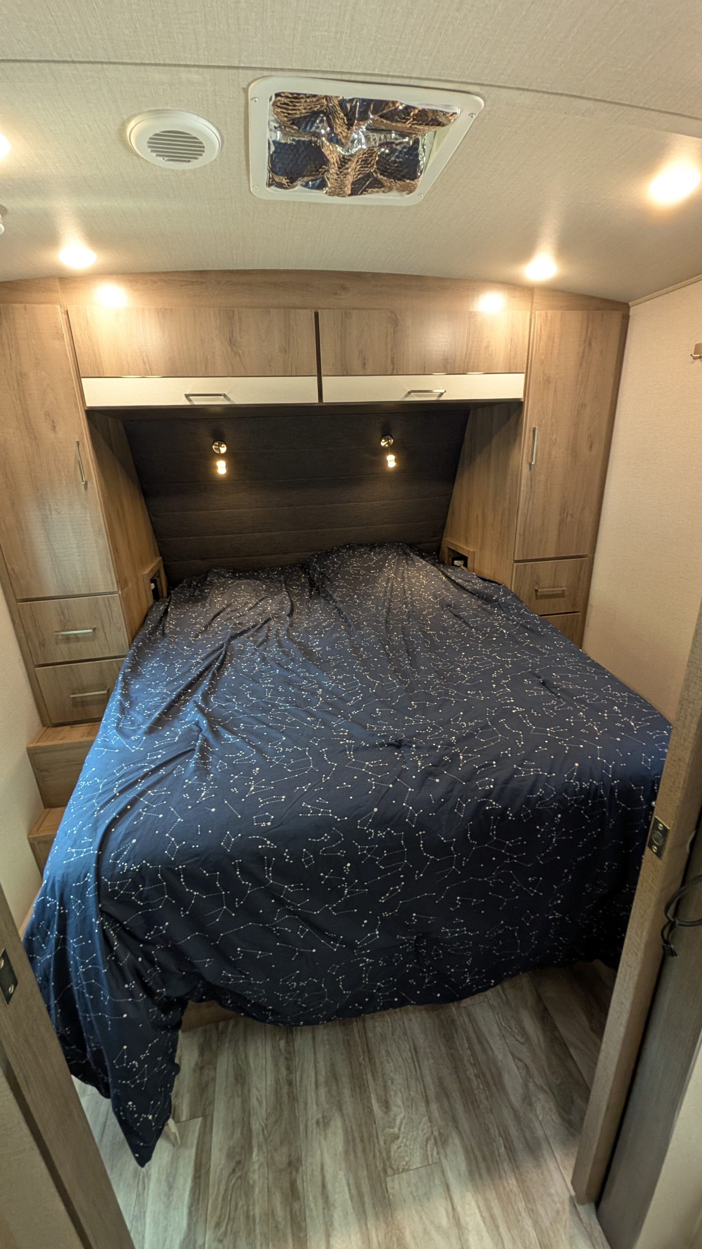 RV rental bedroom featuring constellation bedding, overhead storage, lights, and a ceiling vent/fan.. Grand Design Imagine 2022