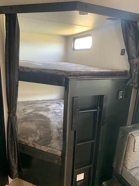 View of cozy bunk beds in an RV rental, complete with soft mattresses, privacy curtains, and a fold-away ladder for top bunk access.. Forest River Cherokee Grey Wolf 2022