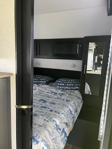 Cozy rv rental bedroom: bed with blue-patterned bedding, dark built-in storage, and mirrored closet.. Forest River Cherokee Grey Wolf 2022