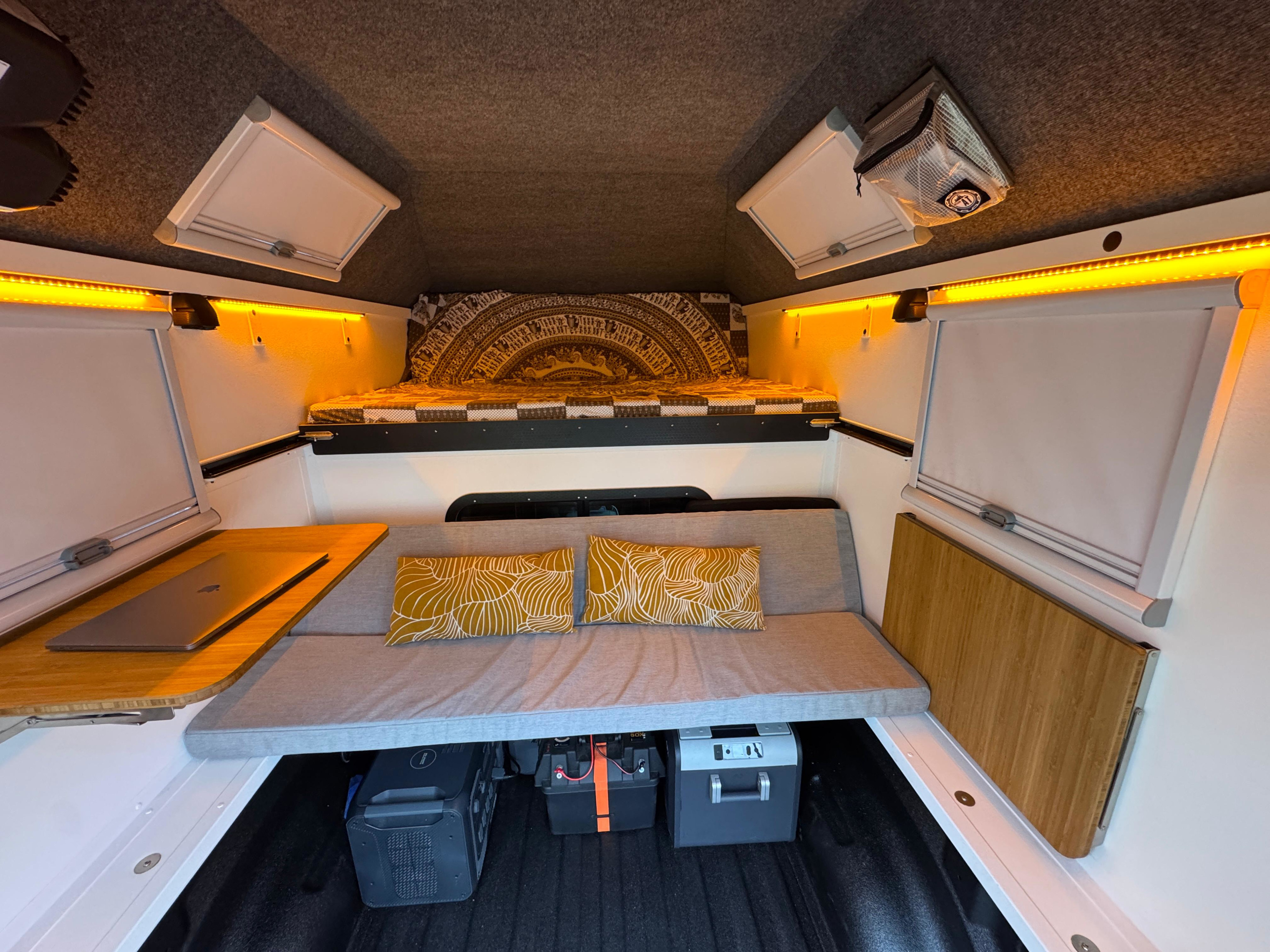 Brightly lit RV rental interior features a bed, sofa, laptop desk, and essential power equipment for comfortable mobile living.. Dodge Ram 1500 2025