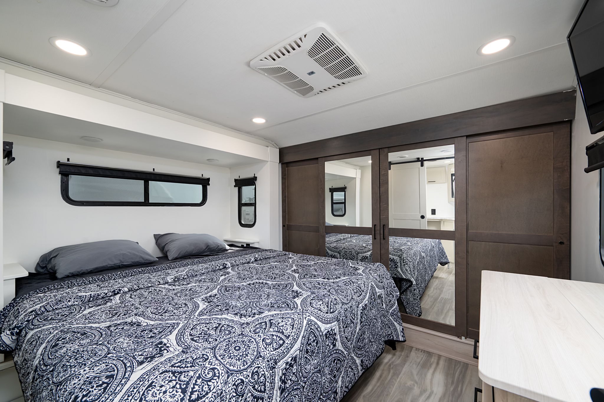 Comfortable RV rental bedroom features a patterned bedspread, practical storage, mirrored closet, and modern amenities.. Alliance RV Valor 2022
