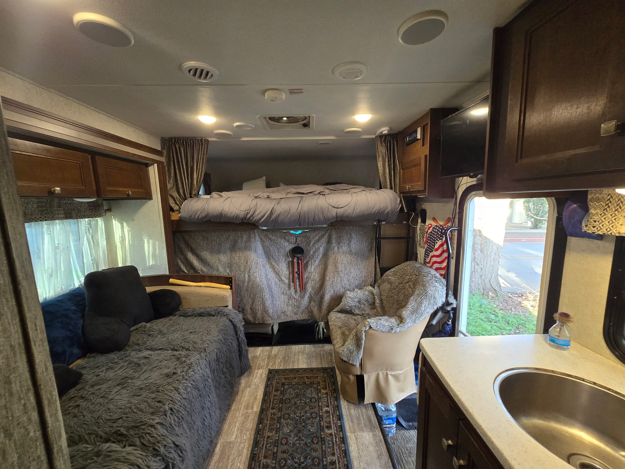 Cozy rv rental interior with bed, sofa, chair, and kitchen sink visible. Warm ceiling lights illuminate the space.. Forest River Sunseeker 2019