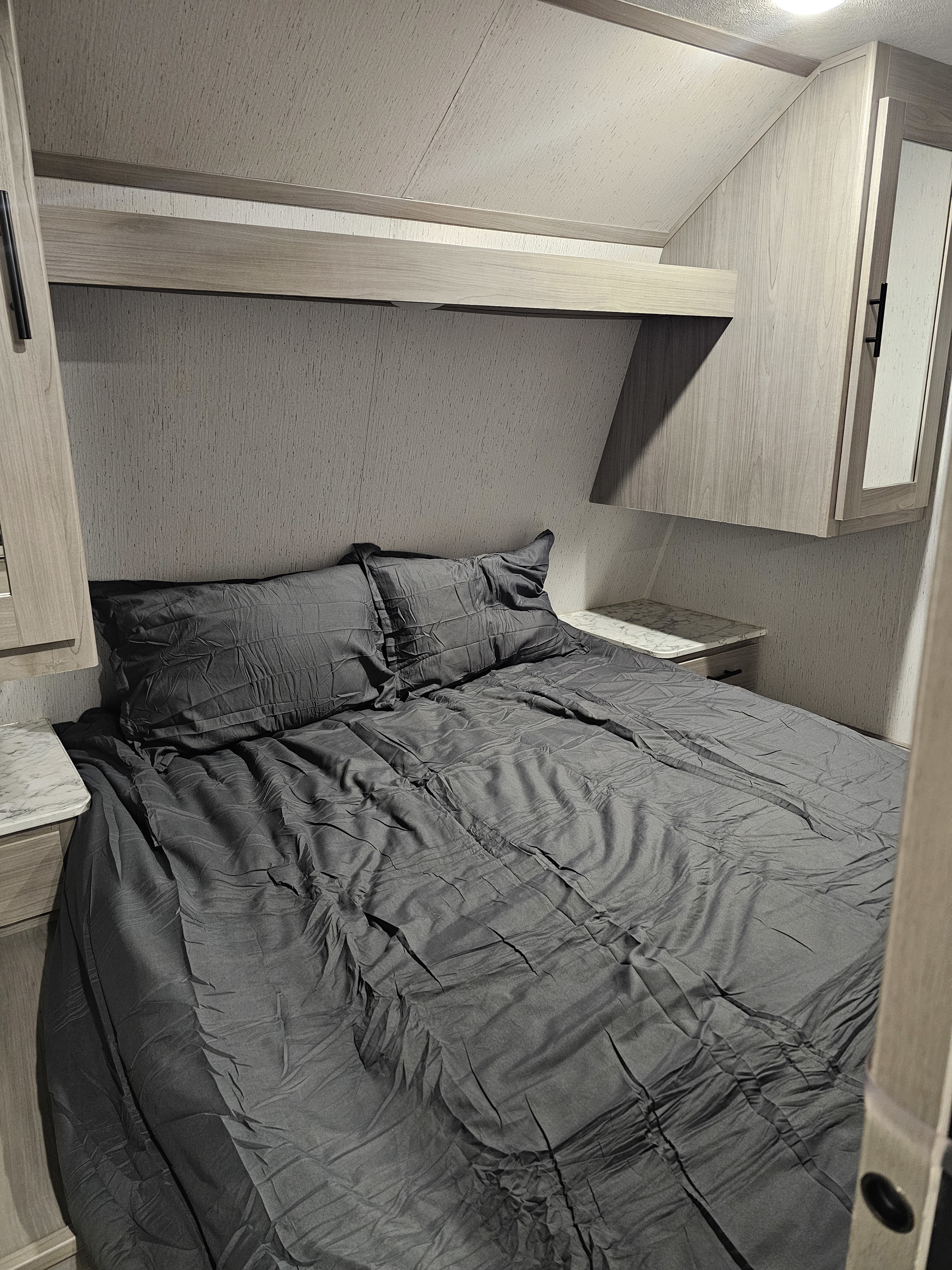 Cozy RV rental bedroom featuring a bed with dark grey bedding, overhead storage, and marble-look nightstands.. Dutchmen Coleman Lantern LT 2022