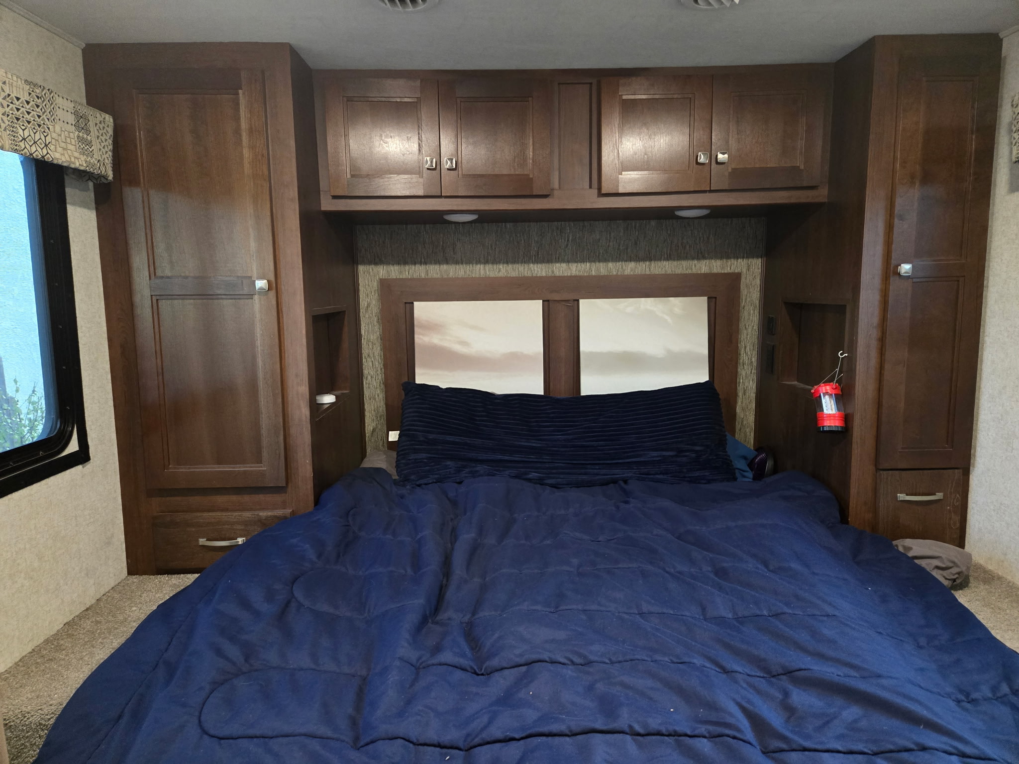 Cozy RV rental bedroom with a comfy bed, blue comforter, dark wood cabinets, and wardrobes, offering ample storage.. Forest River Sunseeker 2019
