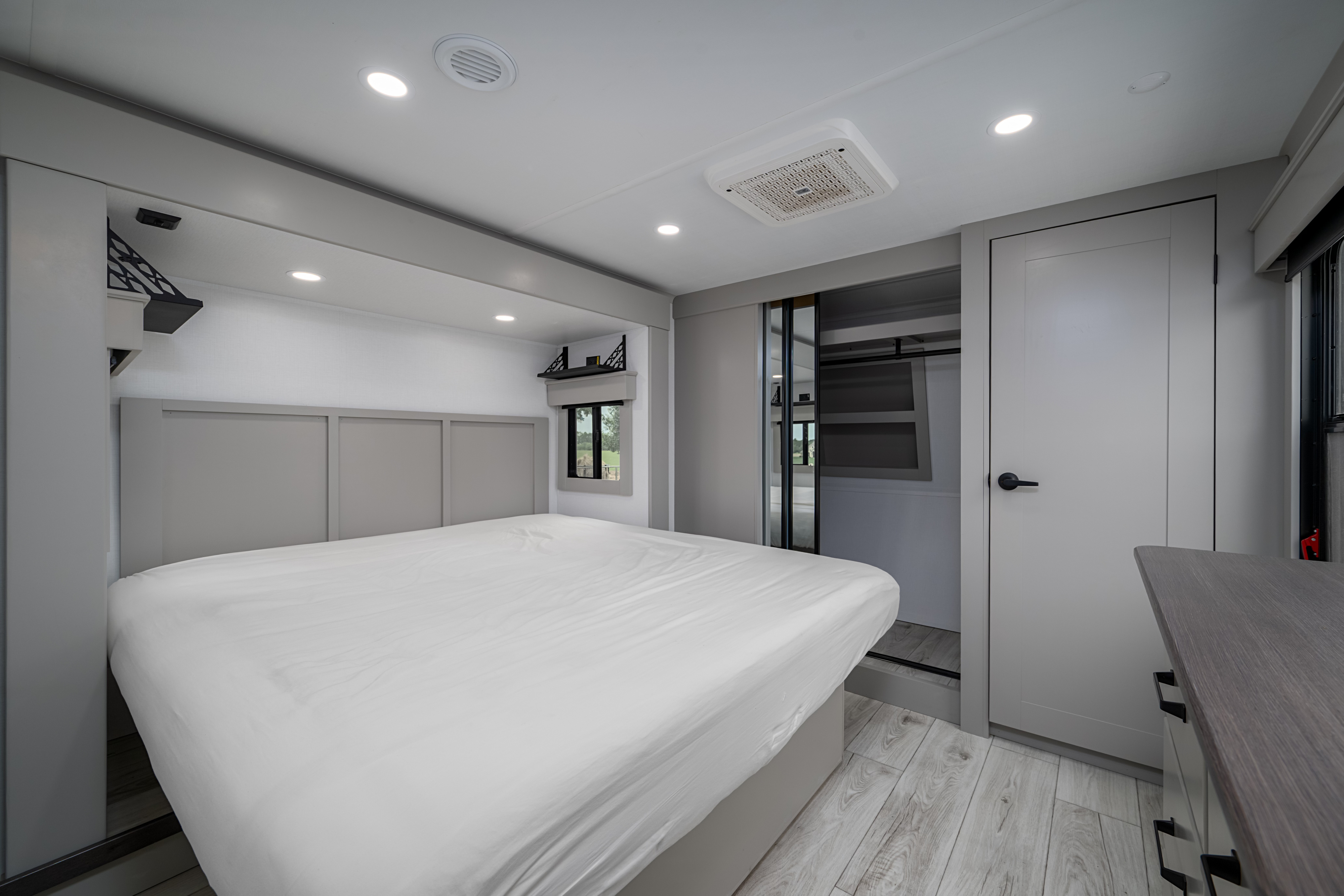 Experience comfort in this modern RV rental bedroom, featuring a large bed, gray headboard, built-in storage, and bright lighting.. Keystone Montana 2025