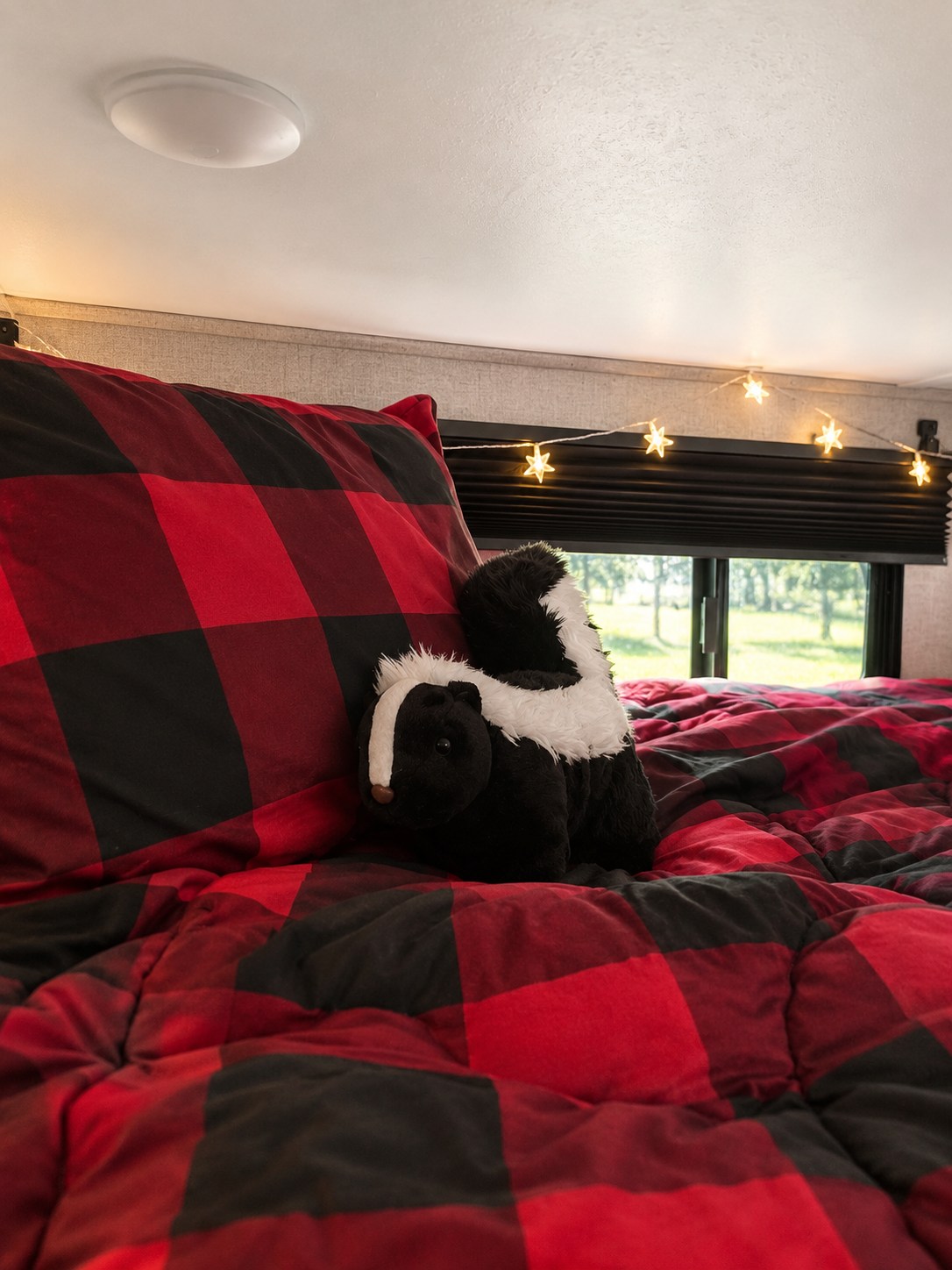 This RV rental features a cozy bedroom with red buffalo plaid bedding, star string lights, and a plush skunk toy.. Coleman Coleman Light LX Series 2125BH 2018