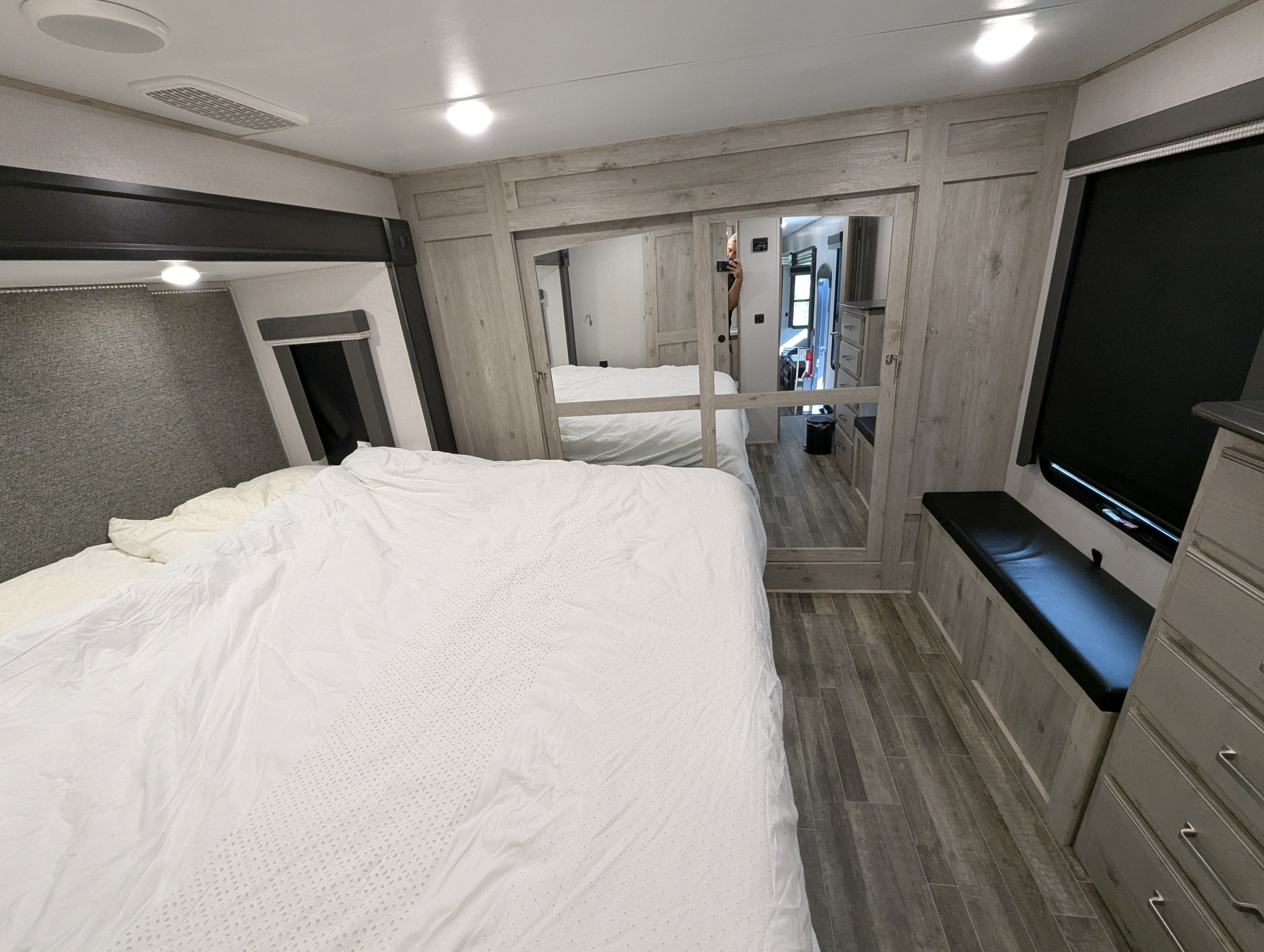 Inside a modern RV rental bedroom featuring a large white bed, mirrored closet, wood-look floor, and a cozy built-in bench.. Keystone Avalanche 2021