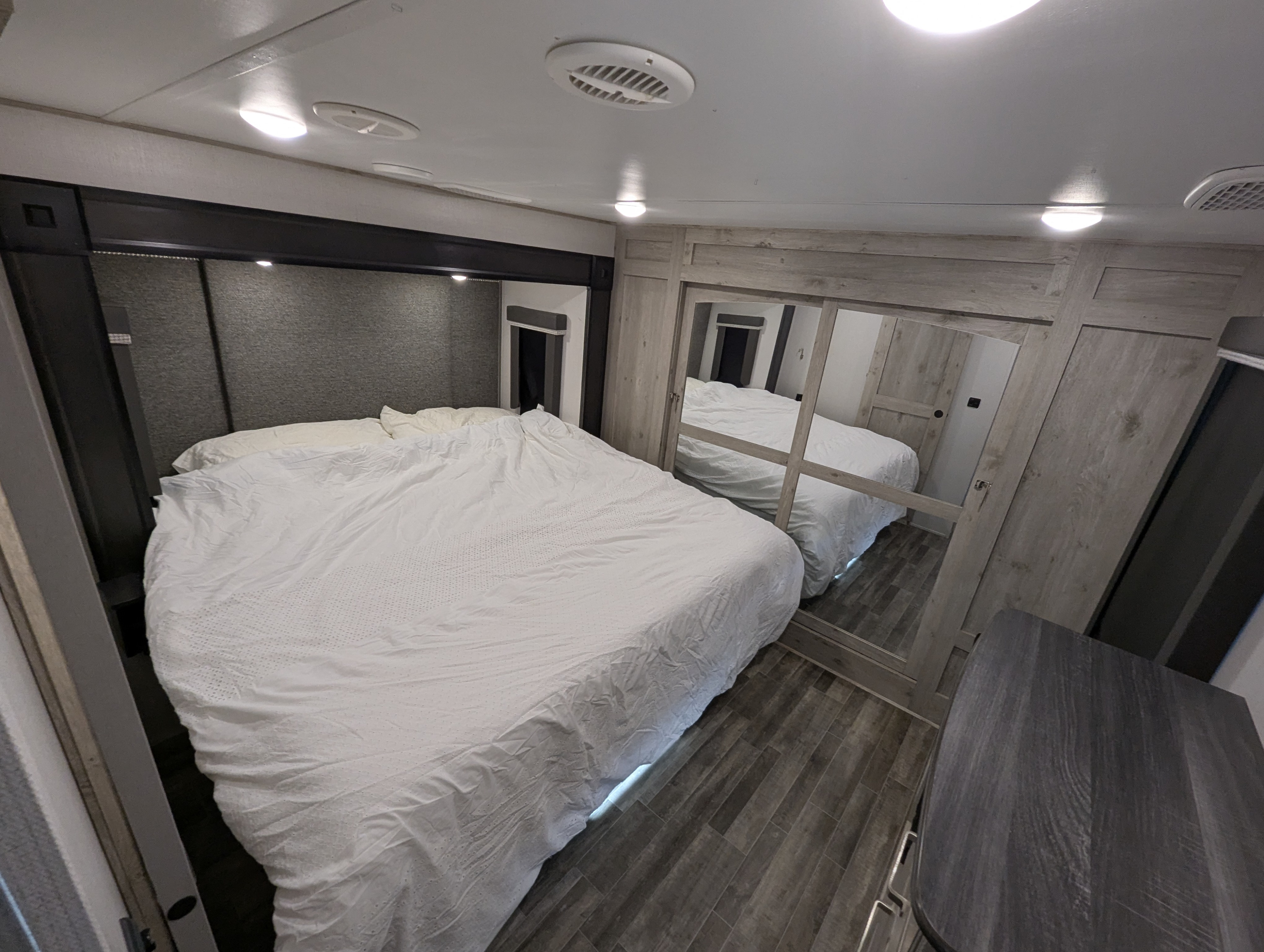 Modern RV rental bedroom with a large bed, crisp white bedding, mirrored closet, and wood-look flooring.. Keystone Avalanche 2021