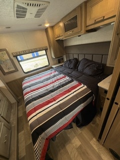 This RV rental bedroom features a spacious bed with a striped comforter, overhead storage, and a window for comfortable travel.. Forest River Coachmen Mirada 2020