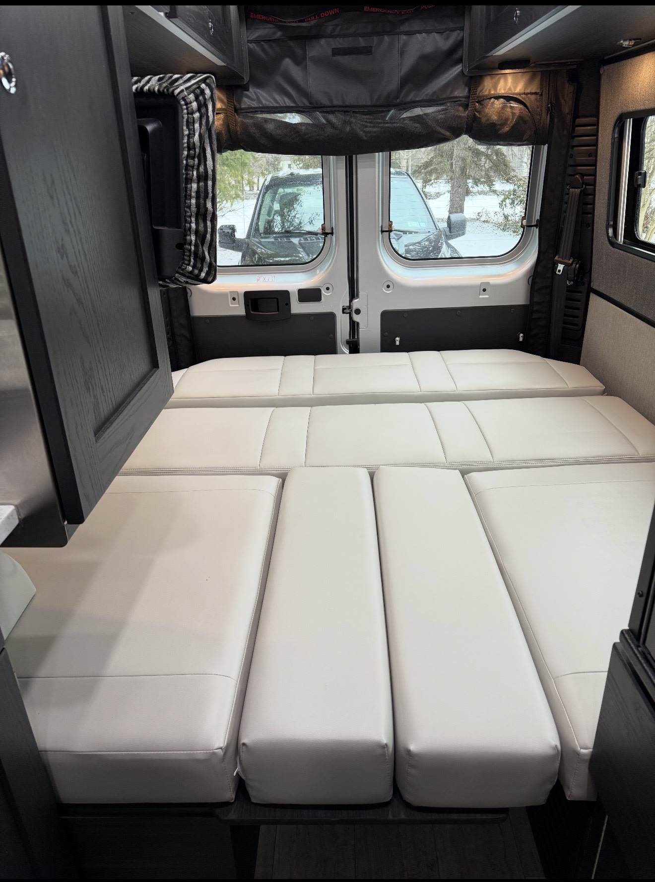 Comfortable white modular bed cushions fill the rear of this RV rental, with winter scenery visible through the back windows.. Roadtrek Zion Slumber 2021