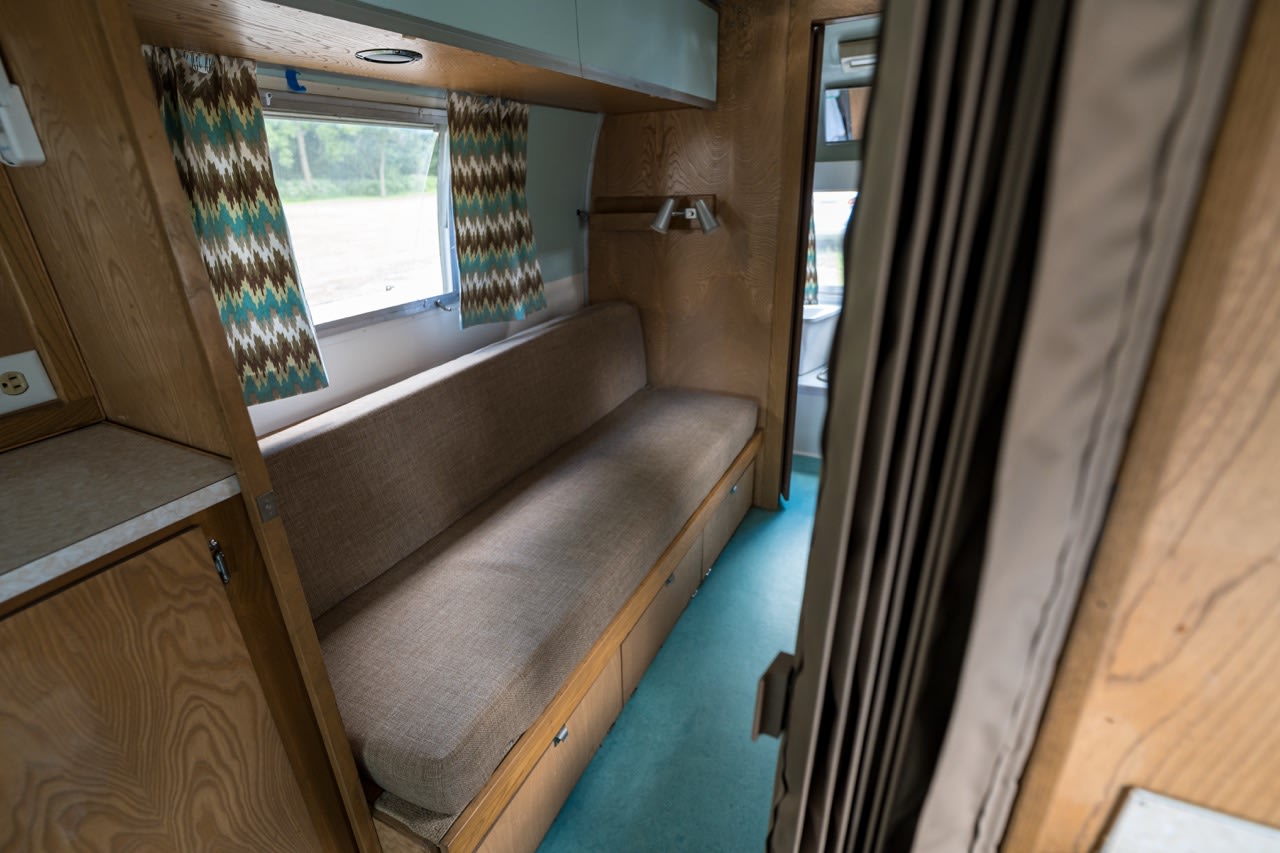 Experience comfort in this RV rental's inviting interior, featuring a long bench seat with storage, windows, and patterned curtains.. Airstream Tradewind 1966